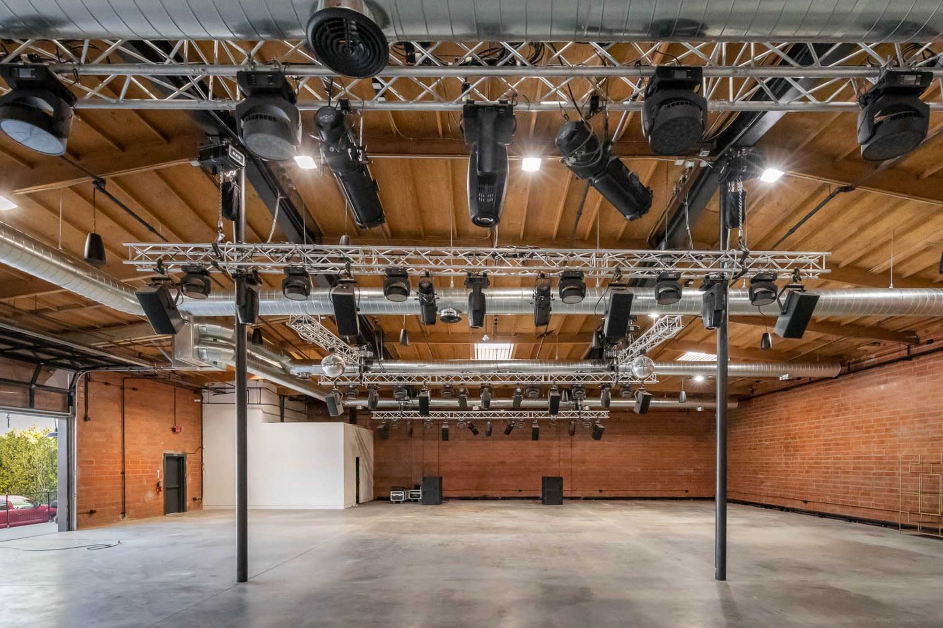 A spacious venue with a wooden ceiling, featuring an array of hanging lights and sound equipment.