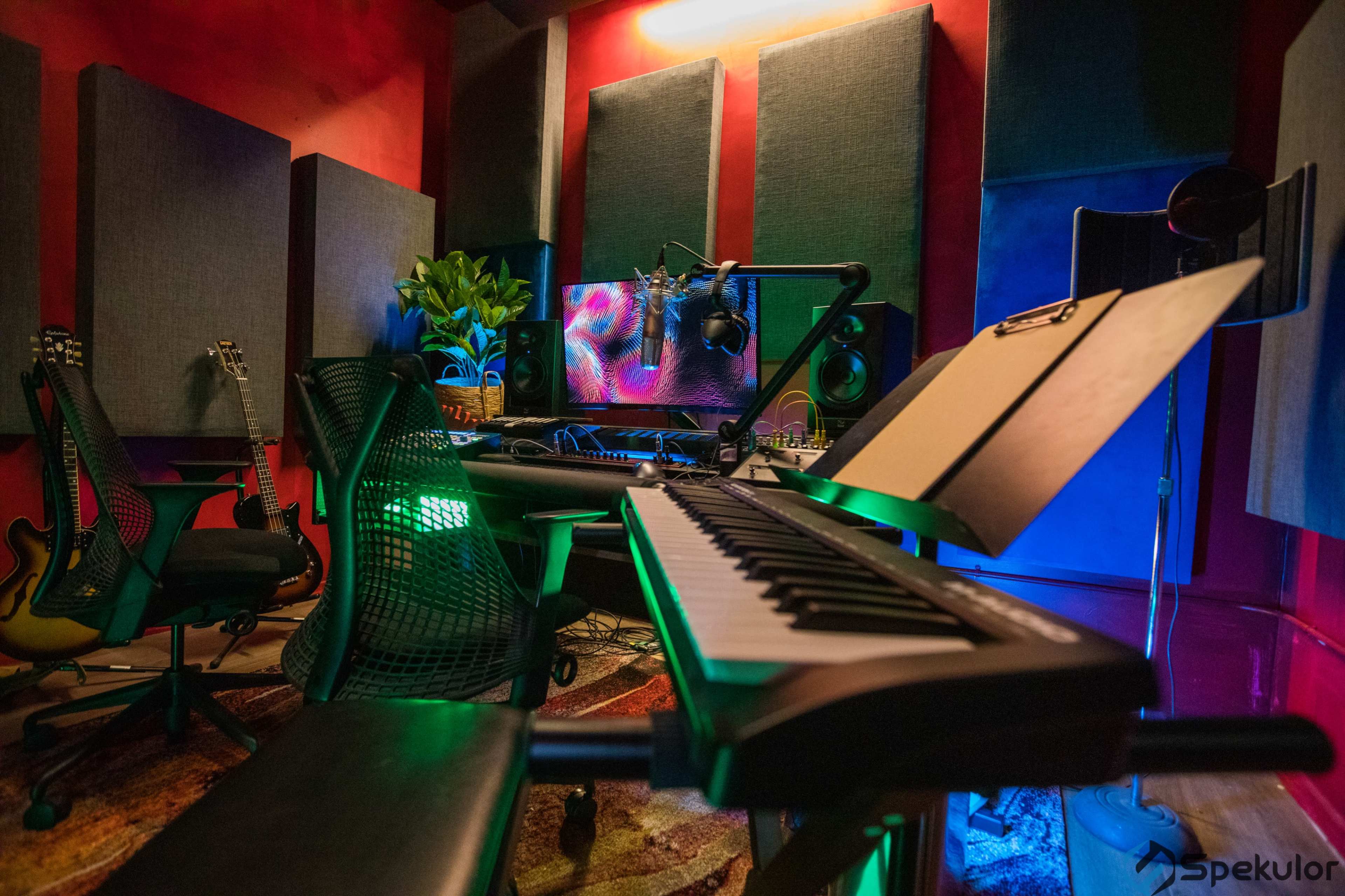 A music studio features a keyboard, chairs, musical instruments, and soundproofing panels against a vibrant backdrop of LED lighting.
