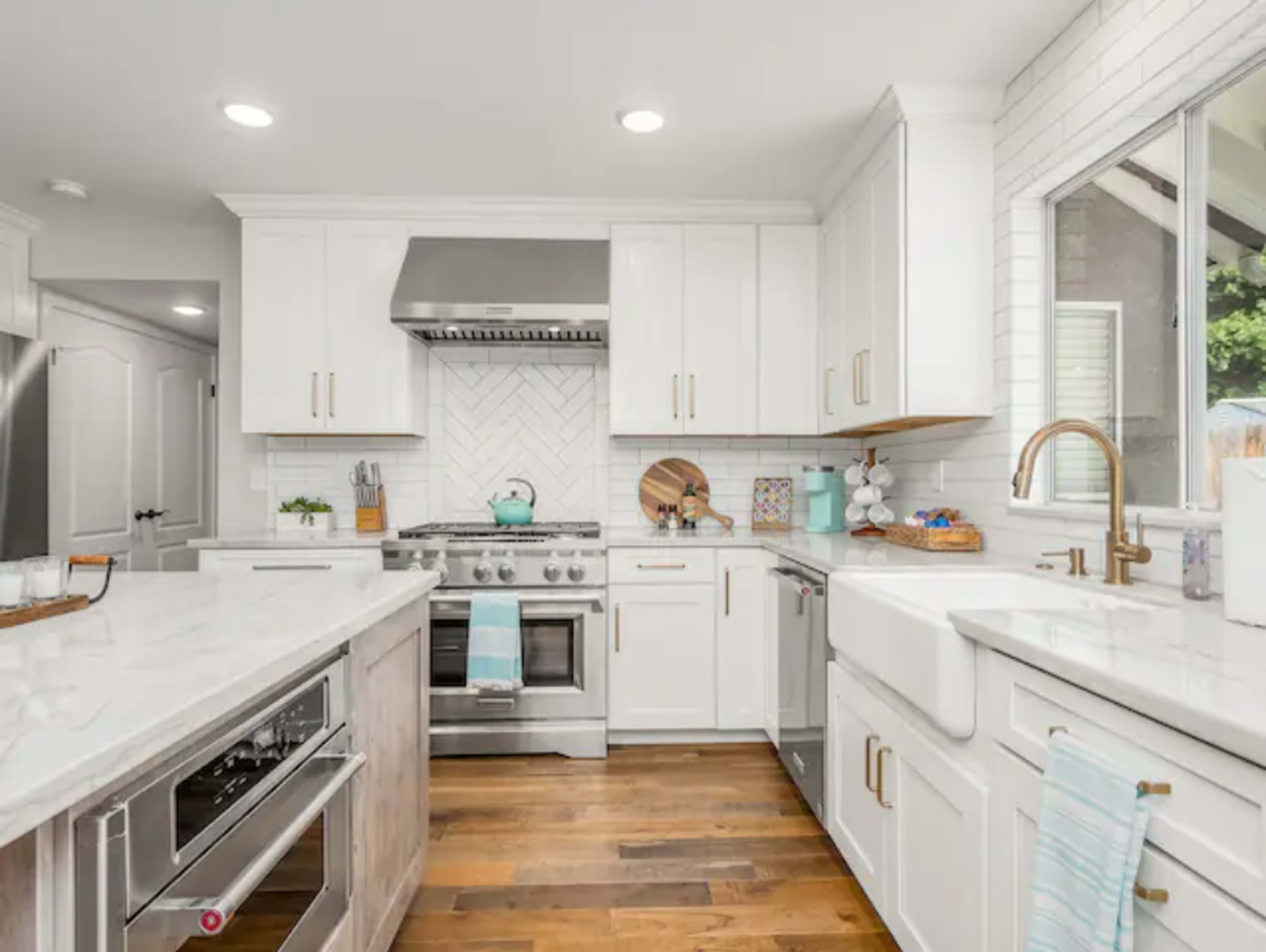 The kitchen features white cabinetry, stainless steel appliances, and a marble countertop with a farm sink and a large window.