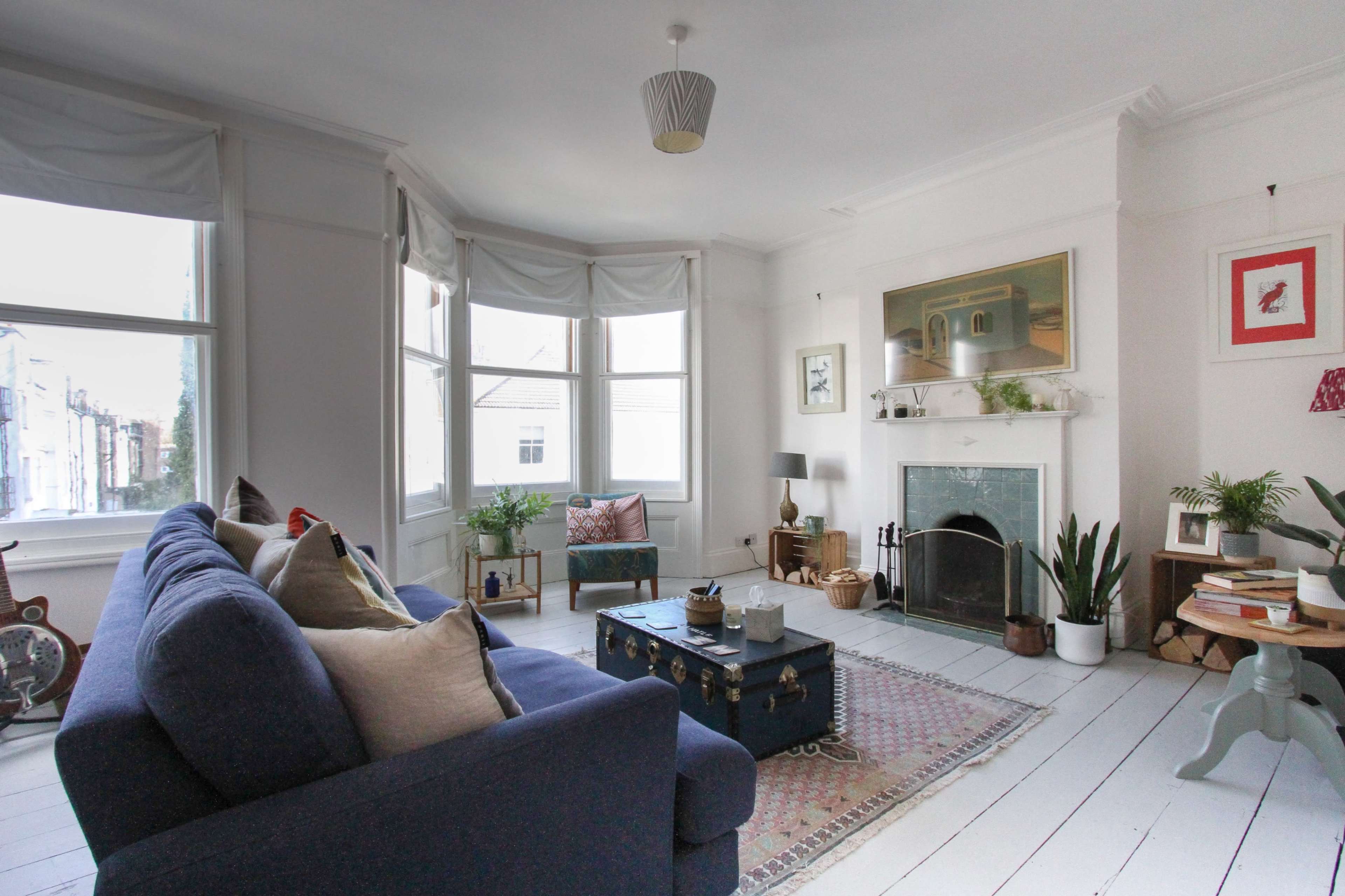 The living room features a blue sofa, a coffee table, and a fireplace, with large windows allowing natural light to fill the space.