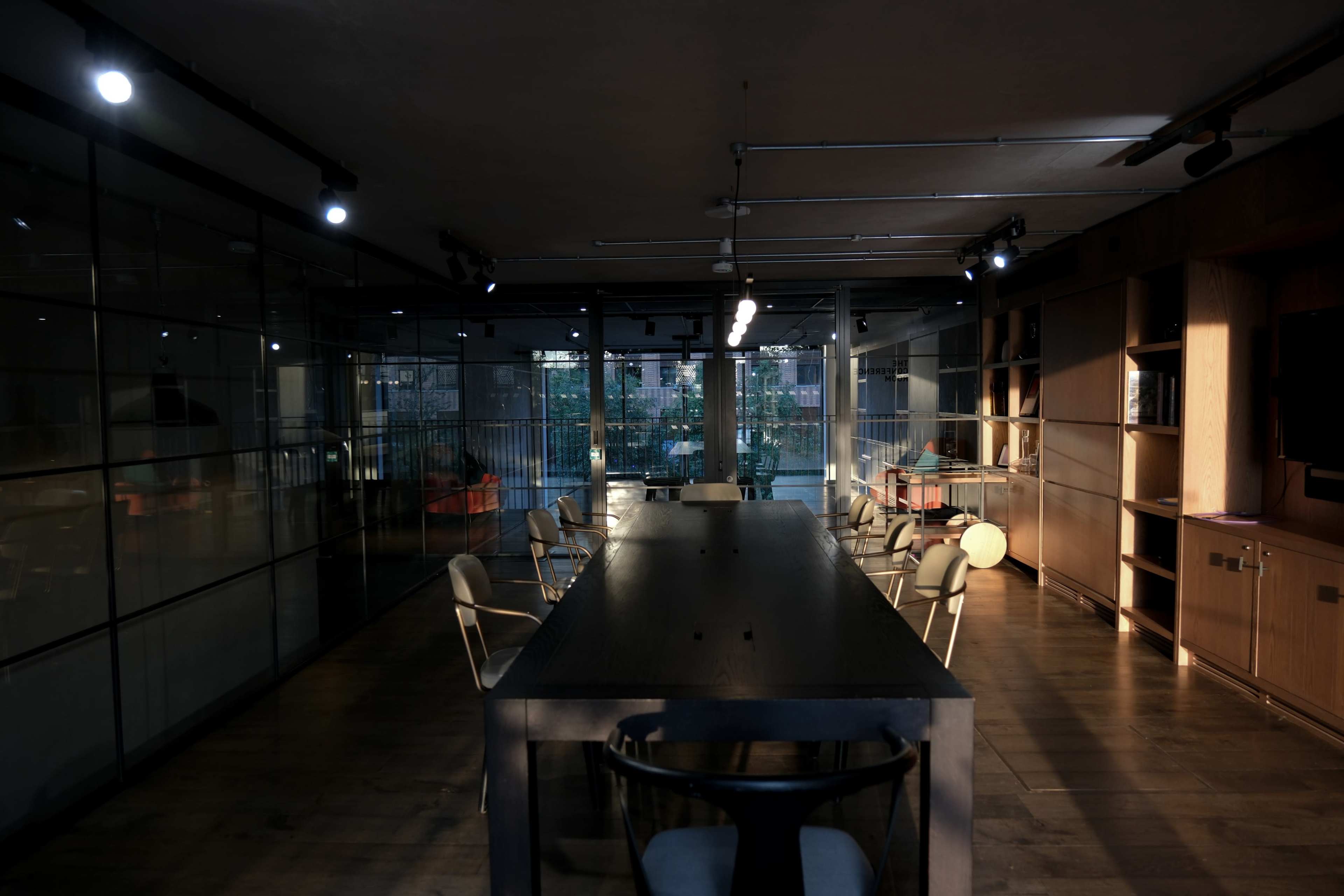 A modern conference room with a long table surrounded by chairs, illuminated by overhead lights.