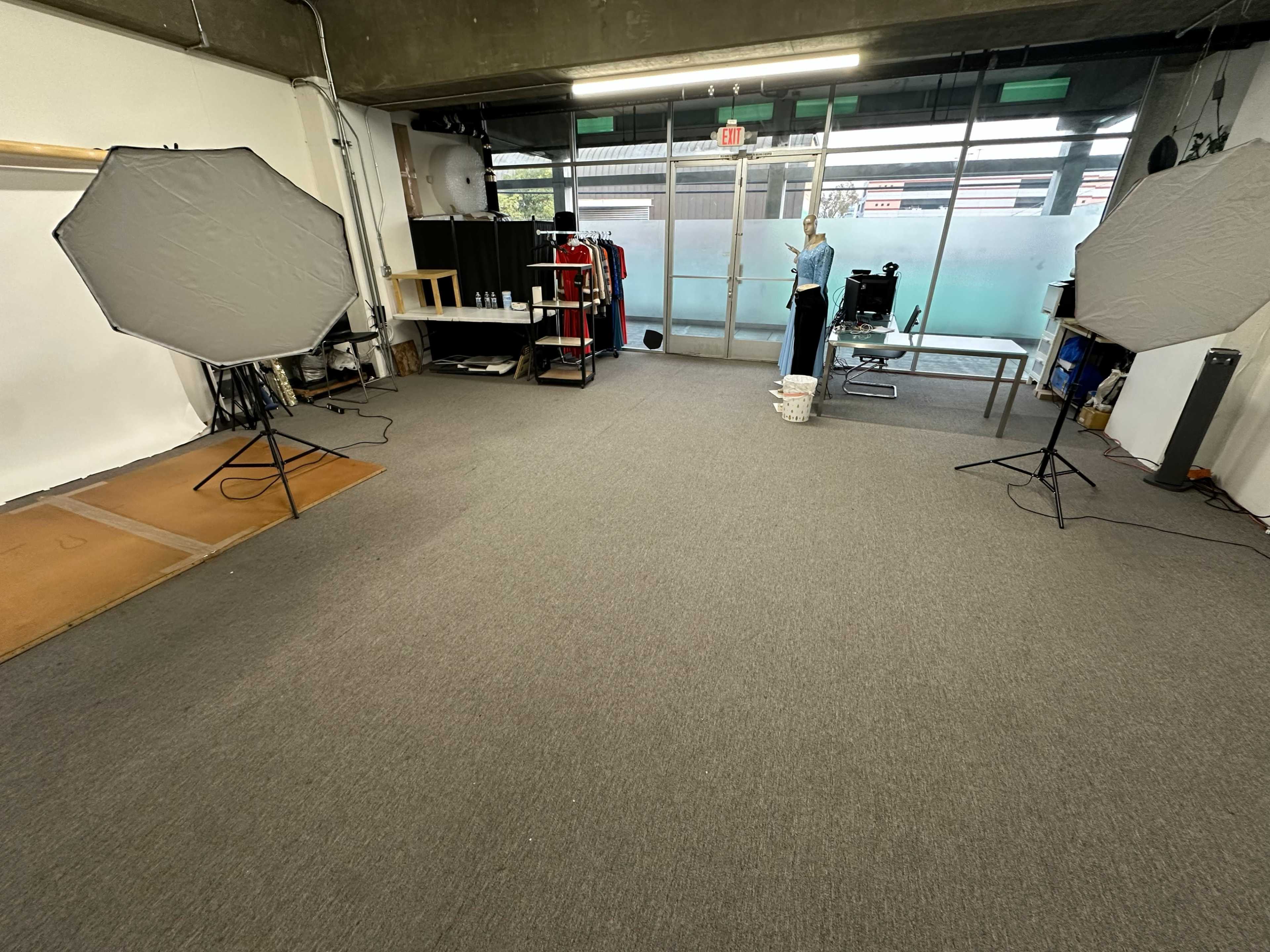 The image shows an empty studio space with two large photography softboxes positioned on tripods, a wooden platform on the floor, and equipment visible in the background.