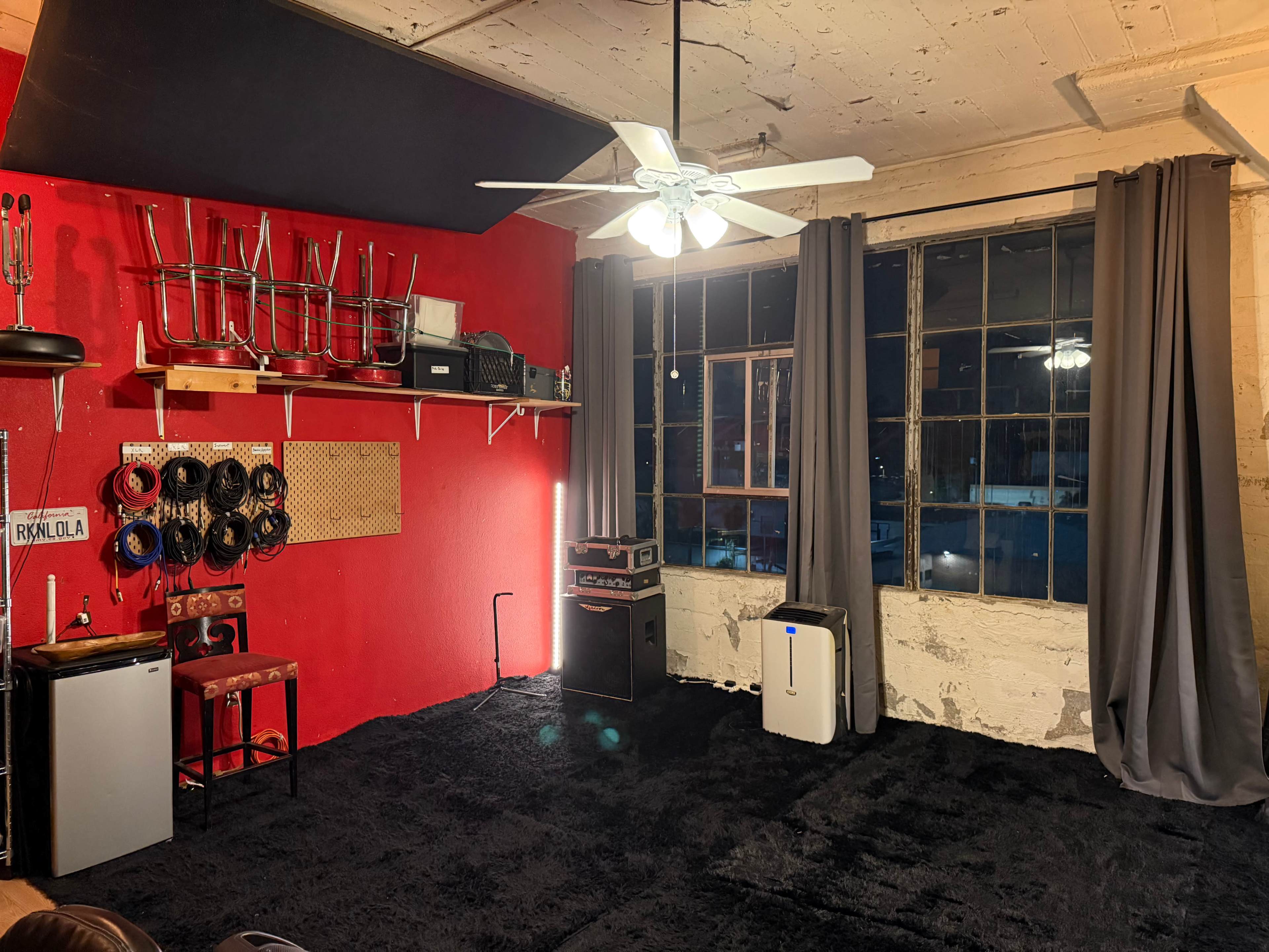 The image shows a room with a red accent wall, carpeted floor, a ceiling fan, and various furniture and equipment along the walls.