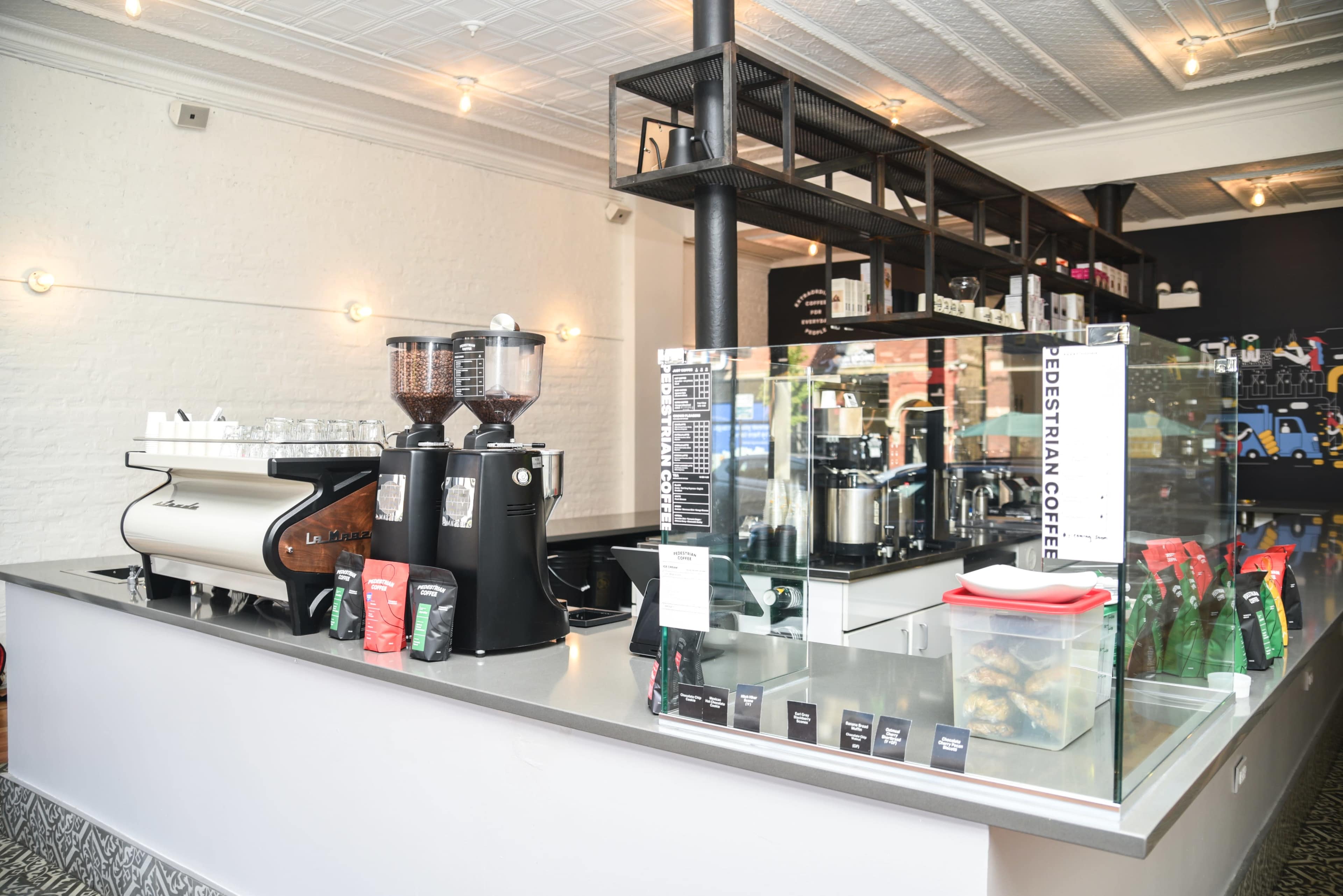 A modern coffee shop interior with a sleek counter featuring an espresso machine, grinders, and neatly arranged coffee bags.