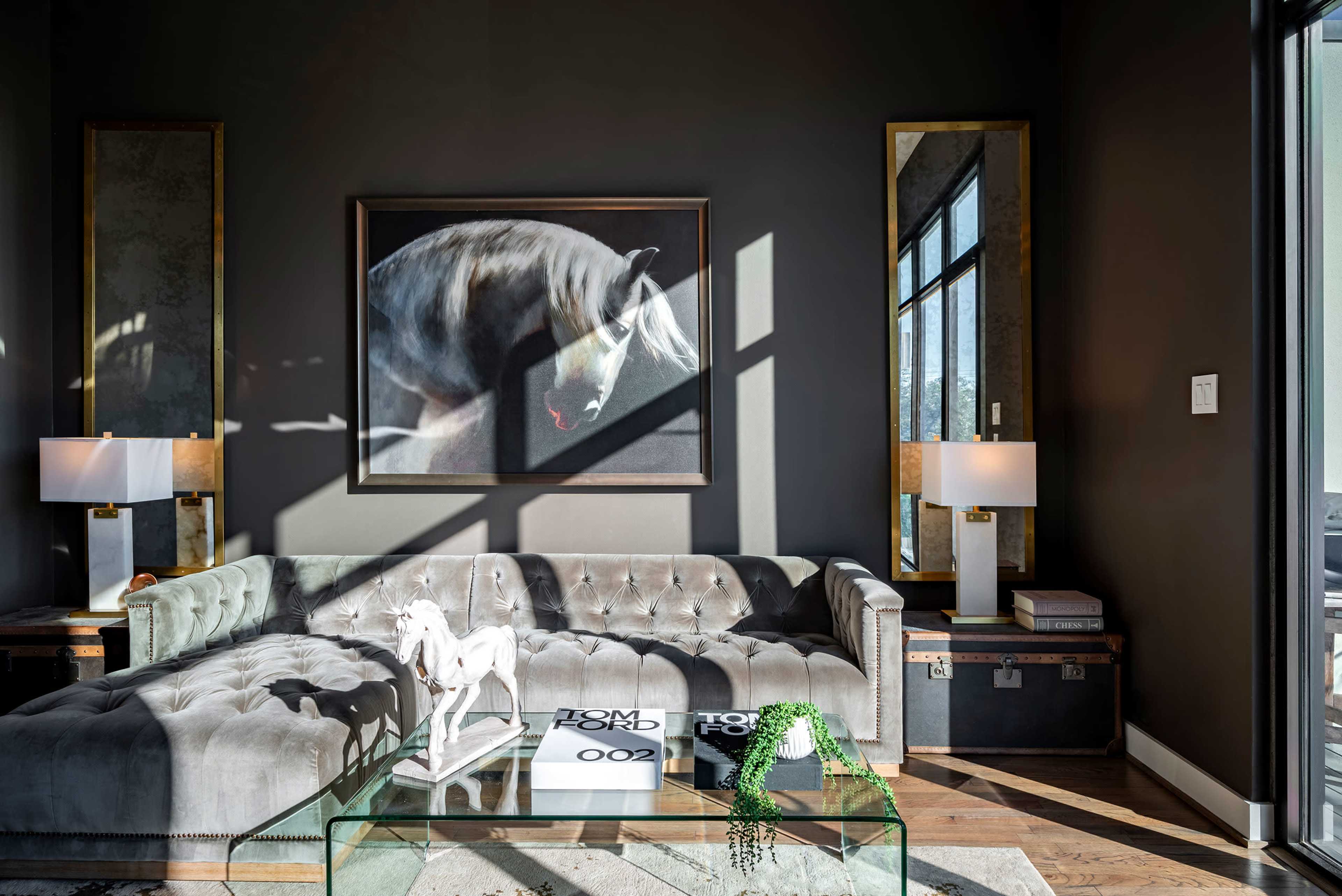 A modern living room features a tufted gray couch, a glass coffee table, and a large painting of a horse hanging on the wall.