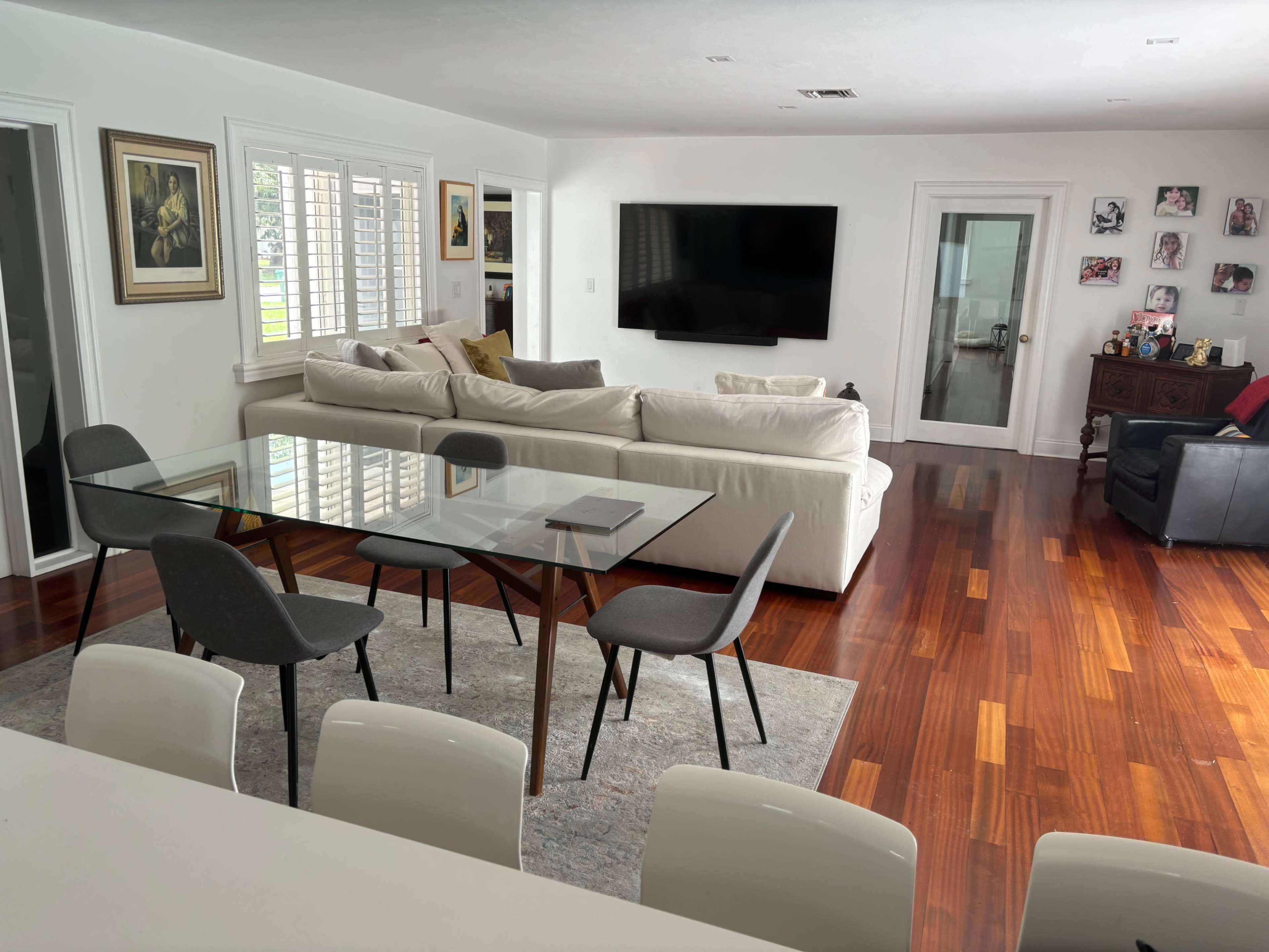 A spacious living area with a glass dining table surrounded by chairs, a large sectional sofa, and a television mounted on the wall.