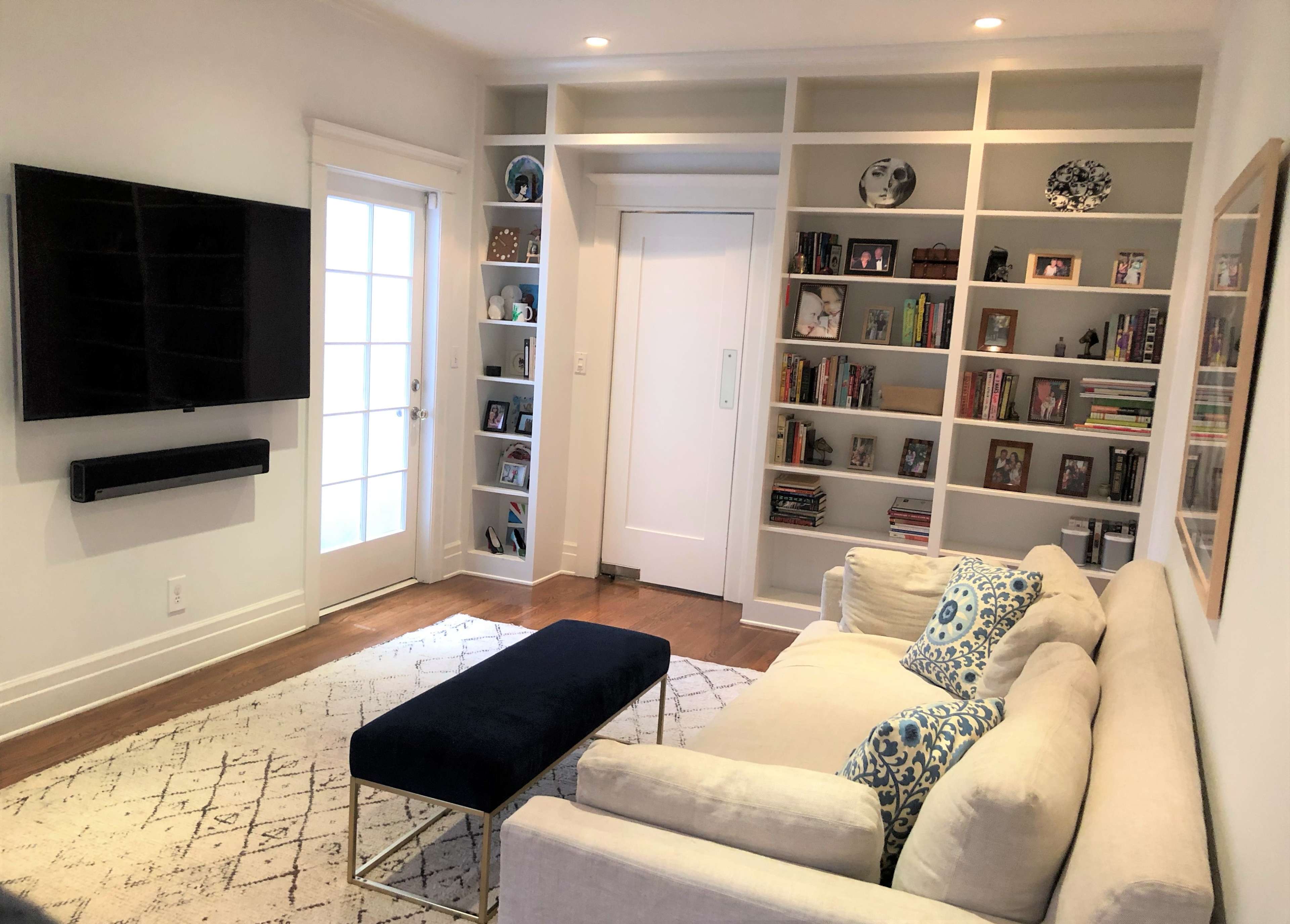 A cozy living room with a sectional sofa facing a wall-mounted television, a coffee table, and built-in shelves filled with books and decorative items.