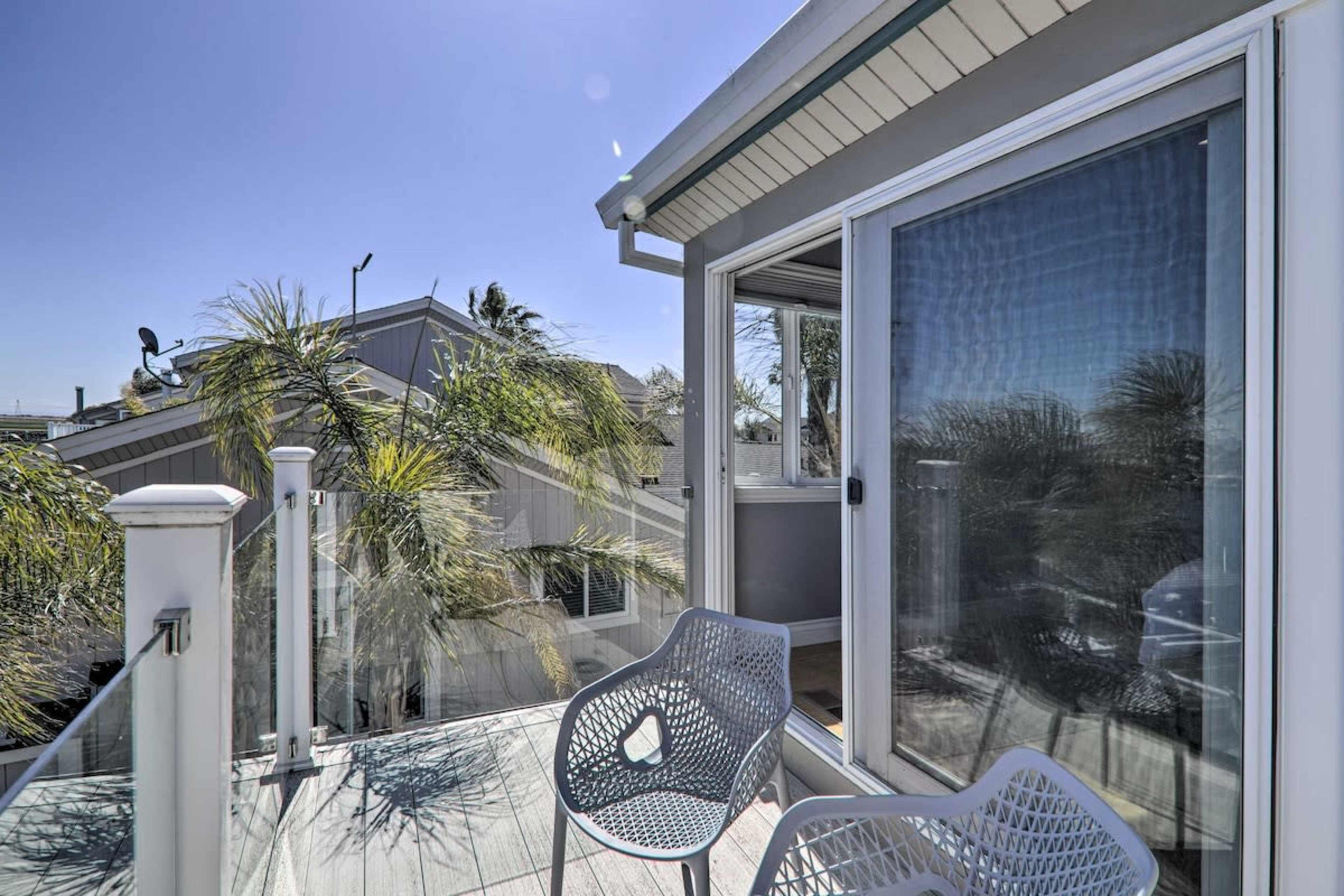 A balcony with two chairs, surrounded by palm trees and a clear blue sky.