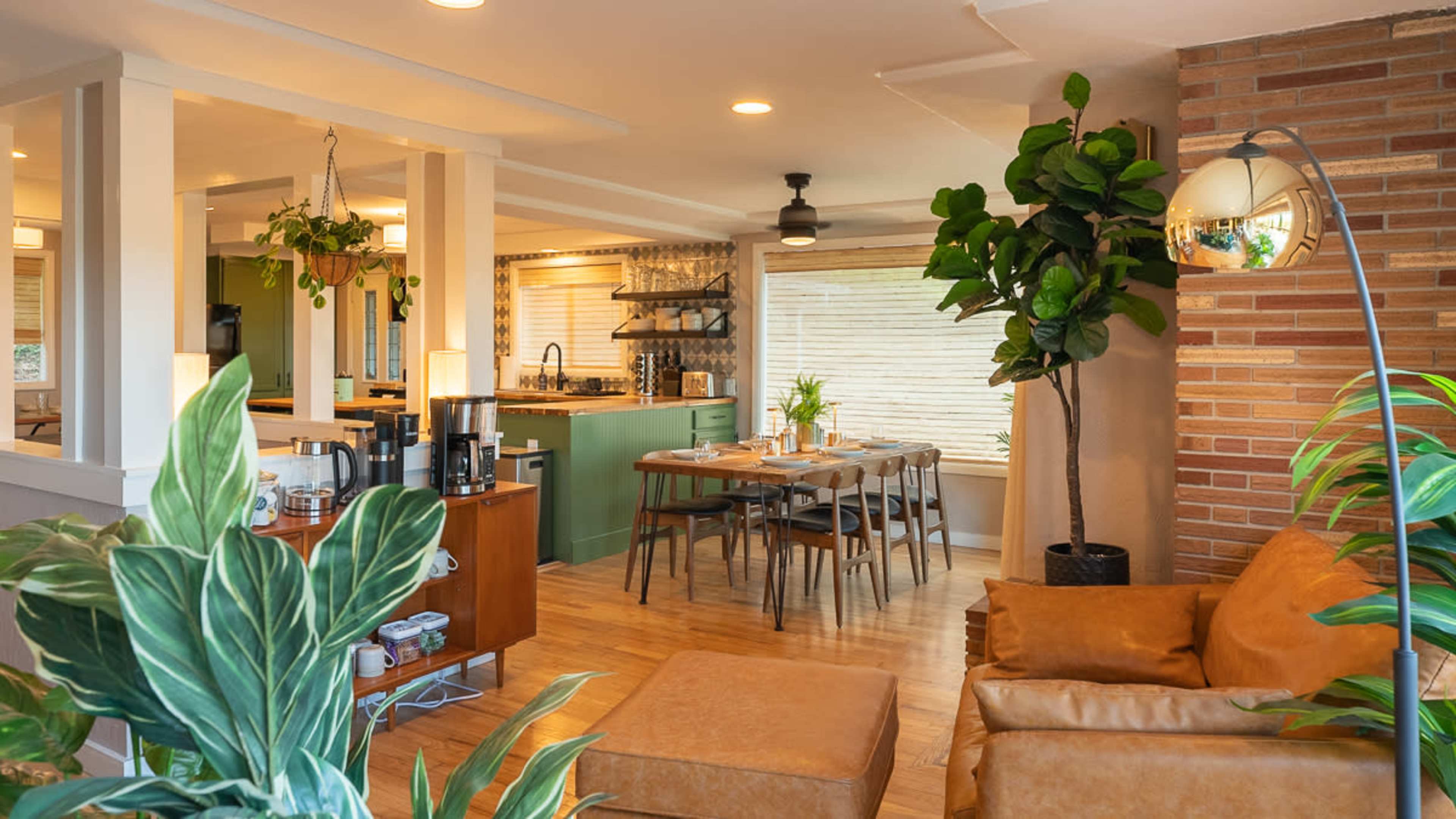 An open-concept living and dining area featuring wooden floors, green kitchen cabinets, a dining table, and potted plants.