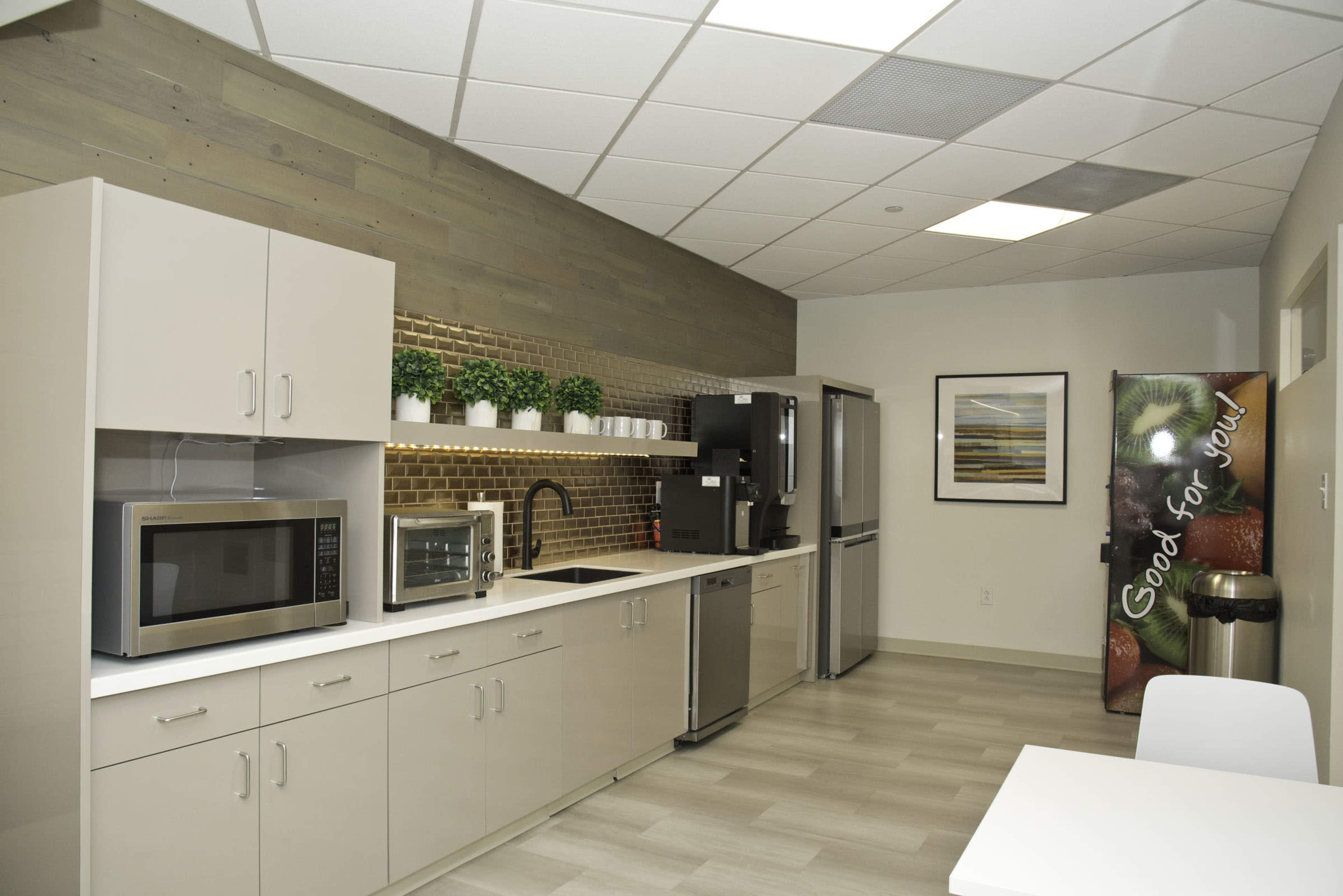 A well-organized kitchen area featuring modern appliances, including a microwave, a refrigerator, and cabinets against a wooden wall with decorative plants.
