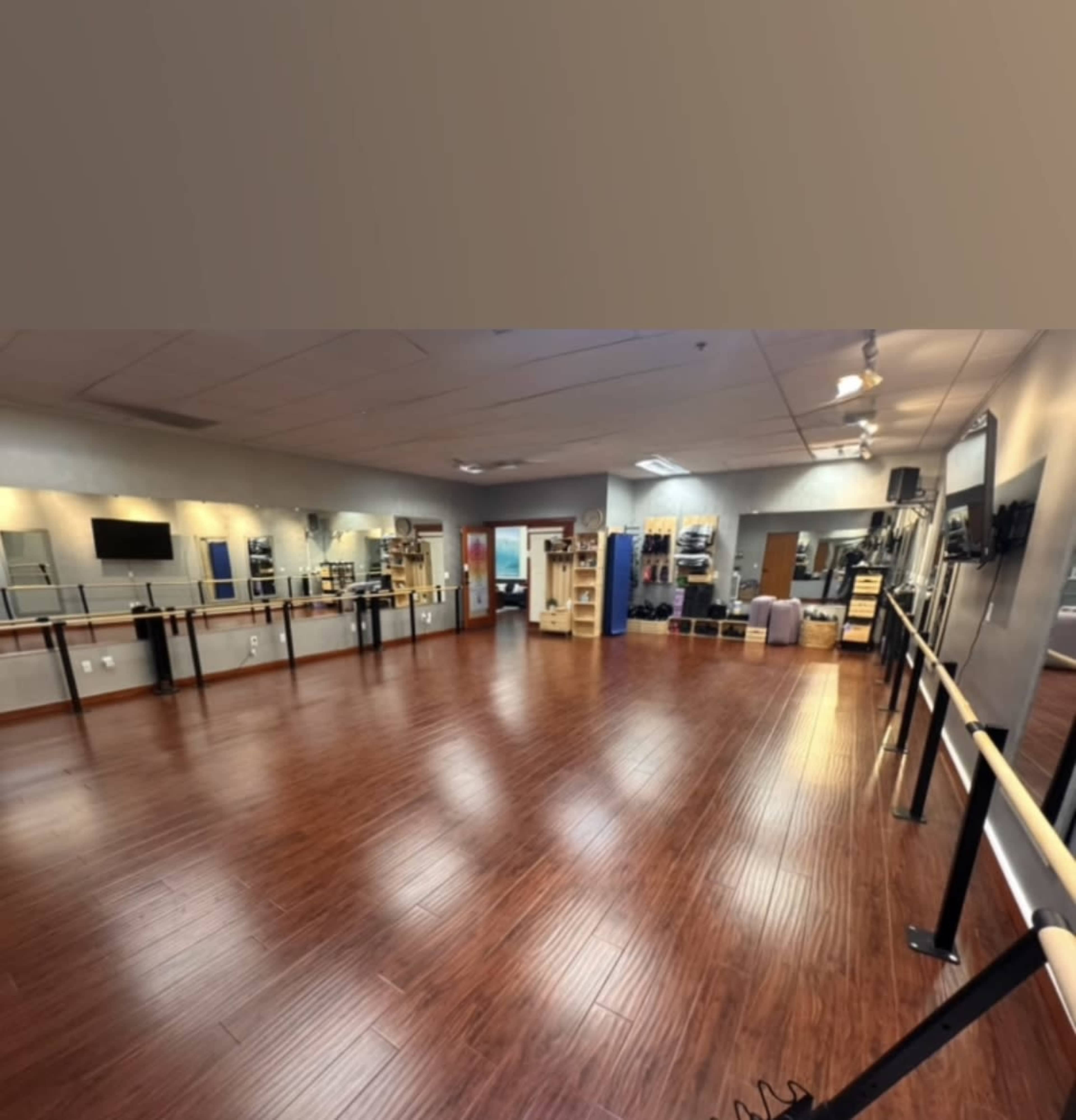 The image depicts a dance studio with wooden flooring, mirrors lining the walls, and a ballet barre along one side.