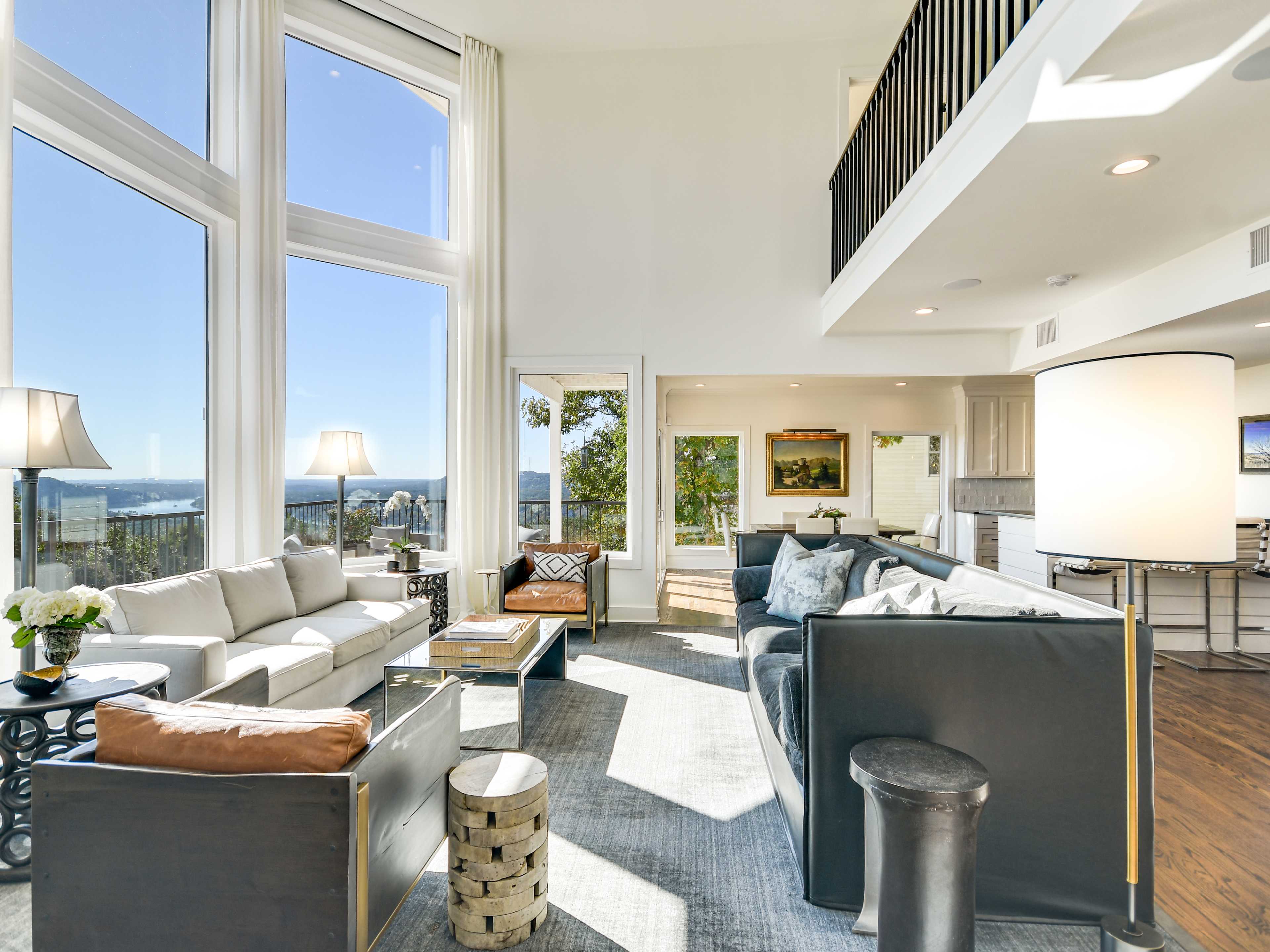 The room features large windows that allow for ample natural light, offering a view of the landscape beyond, with modern furniture arranged around a central area.