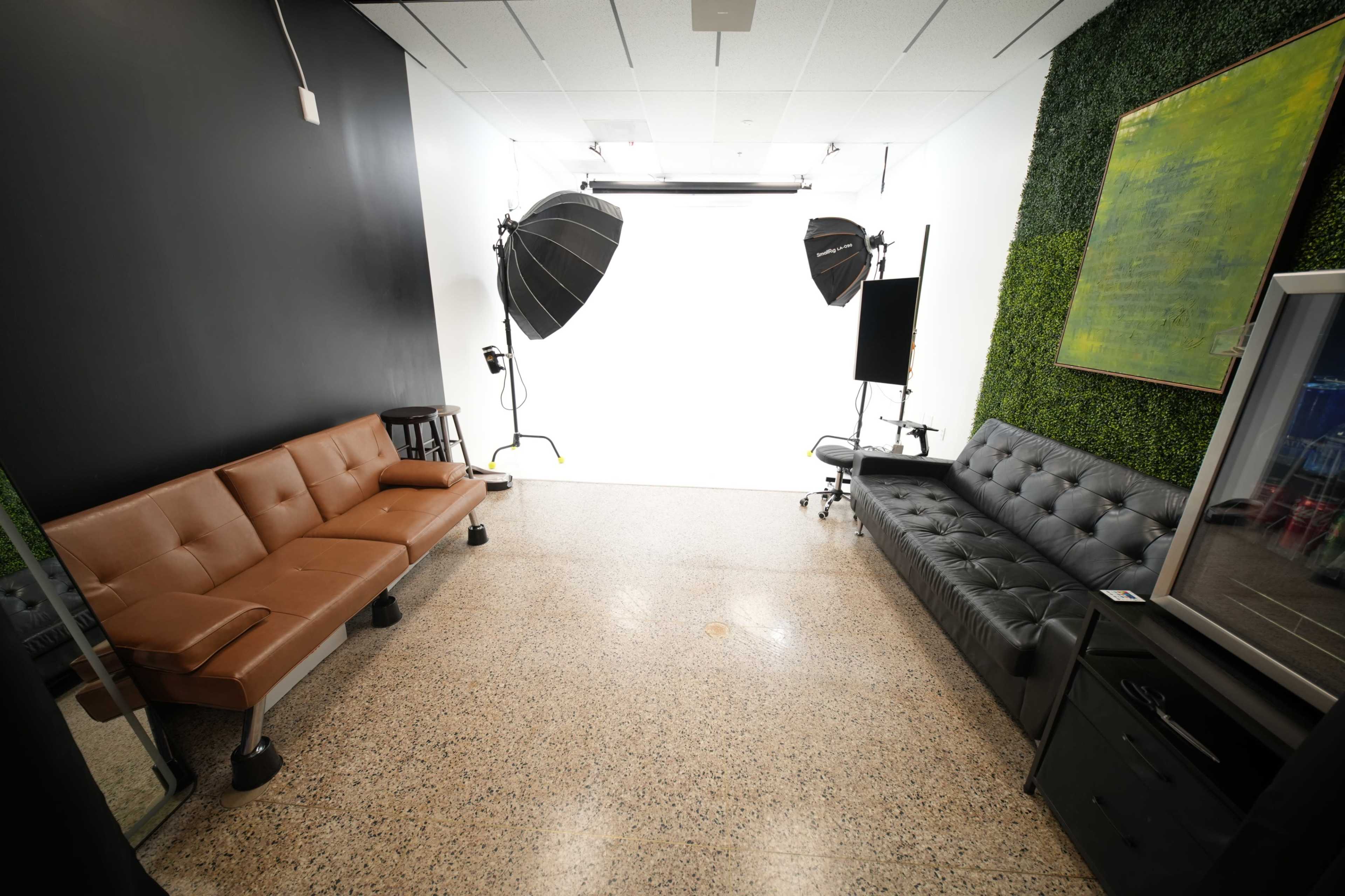 The image shows a photography studio with two different style couches, a large mirror, and studio lighting equipment set against a blank white wall.