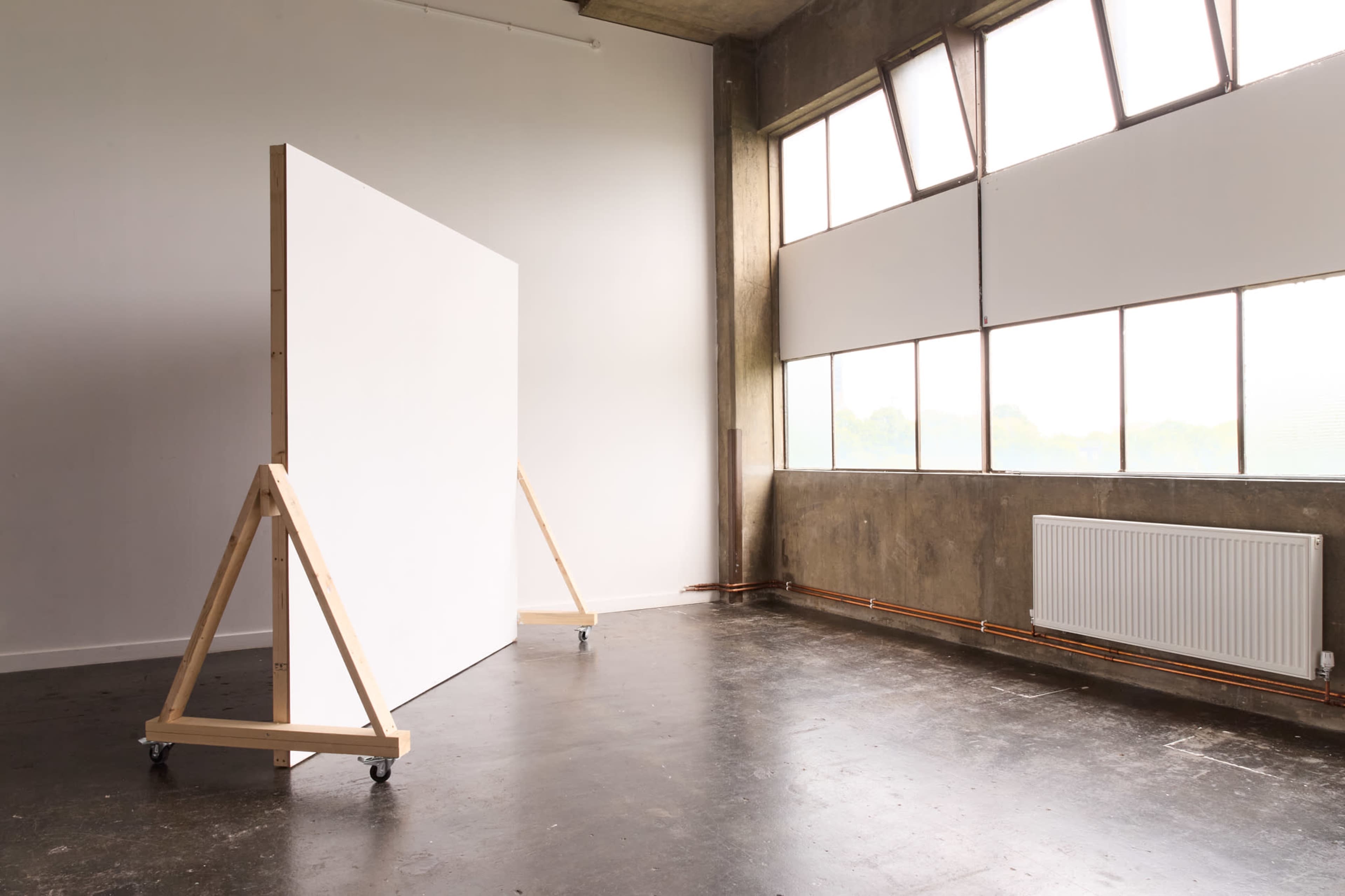 A spacious room with a large white canvas on a wooden easel and large windows allowing natural light to enter.