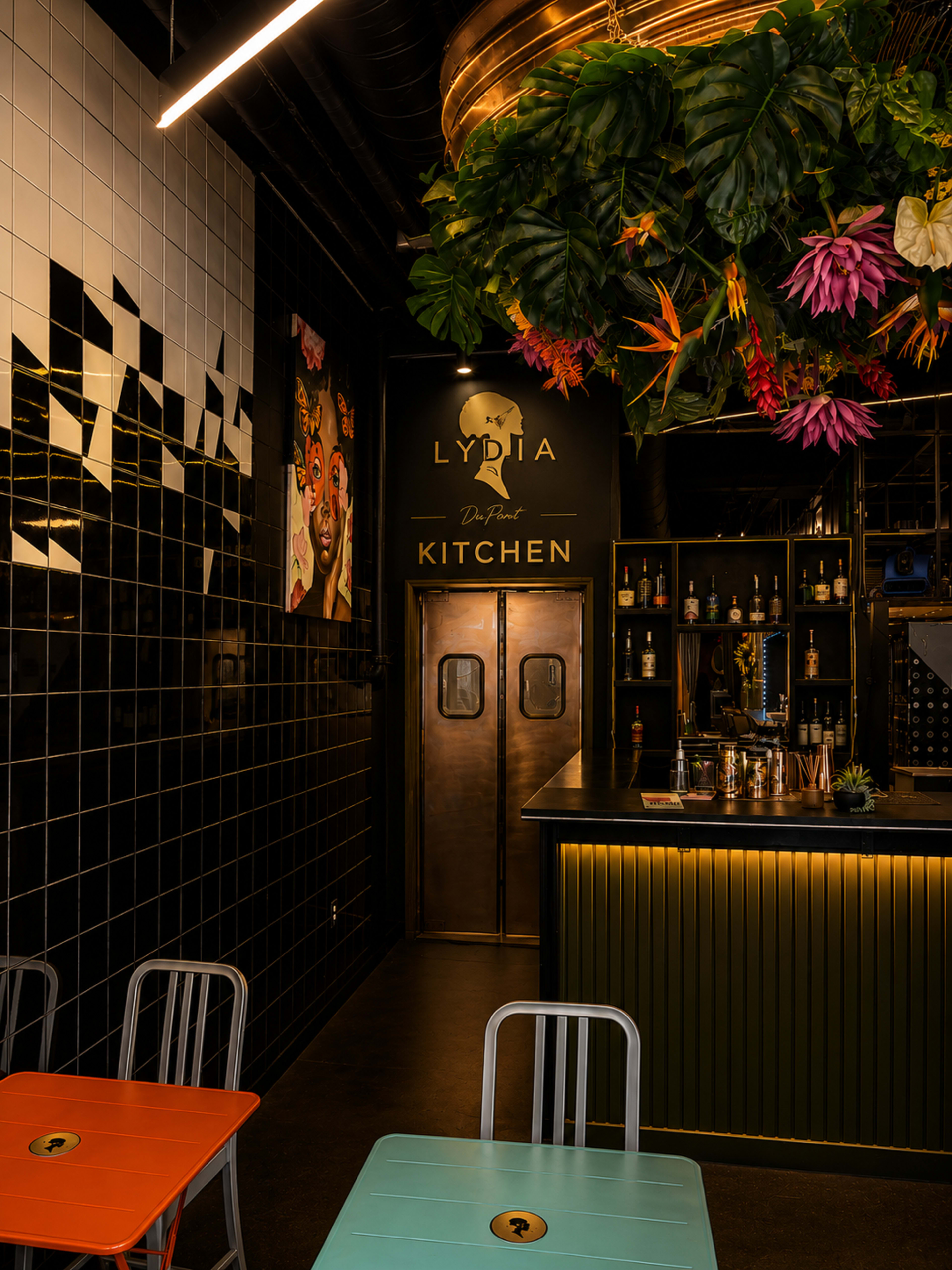 The image shows the interior of a restaurant named "Lydia Kitchen," featuring colorful furniture, a bar area, and tropical plants suspended from the ceiling.