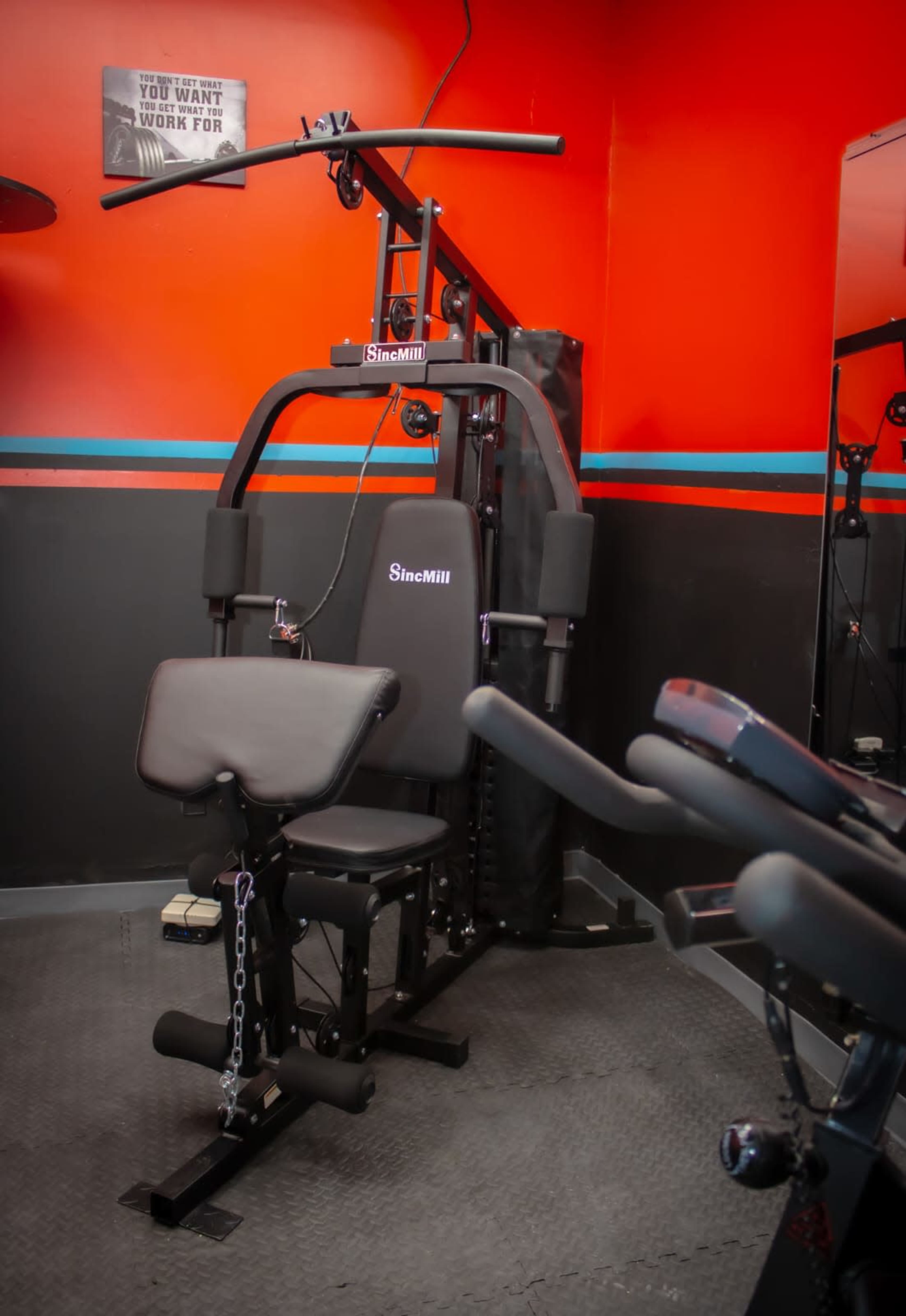 A gym setup featuring a cable machine against a red wall, with a bench and various attachments for strength training.