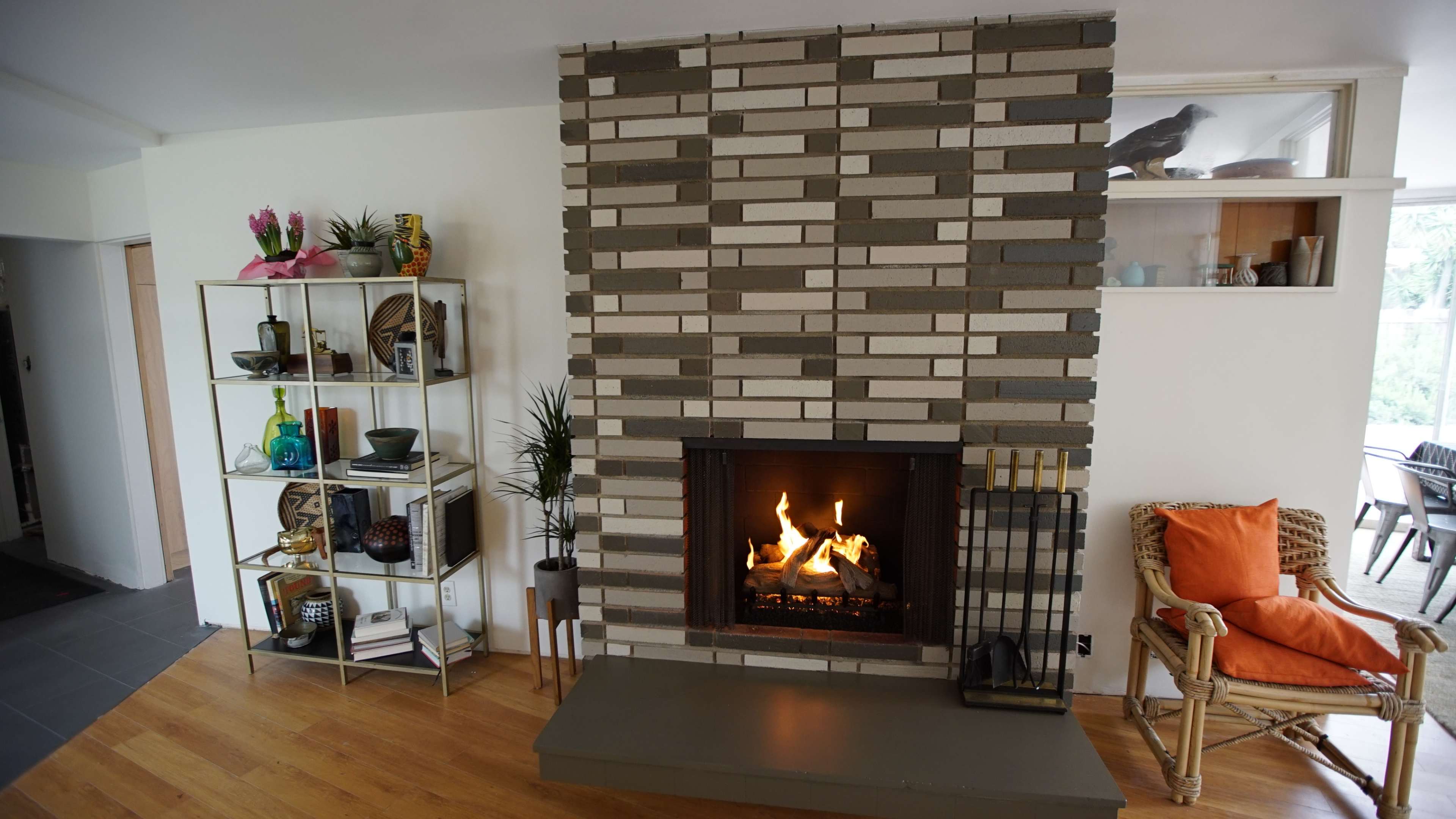 A modern living room with a stone fireplace, a metal shelving unit filled with decorative items, and a rattan chair.