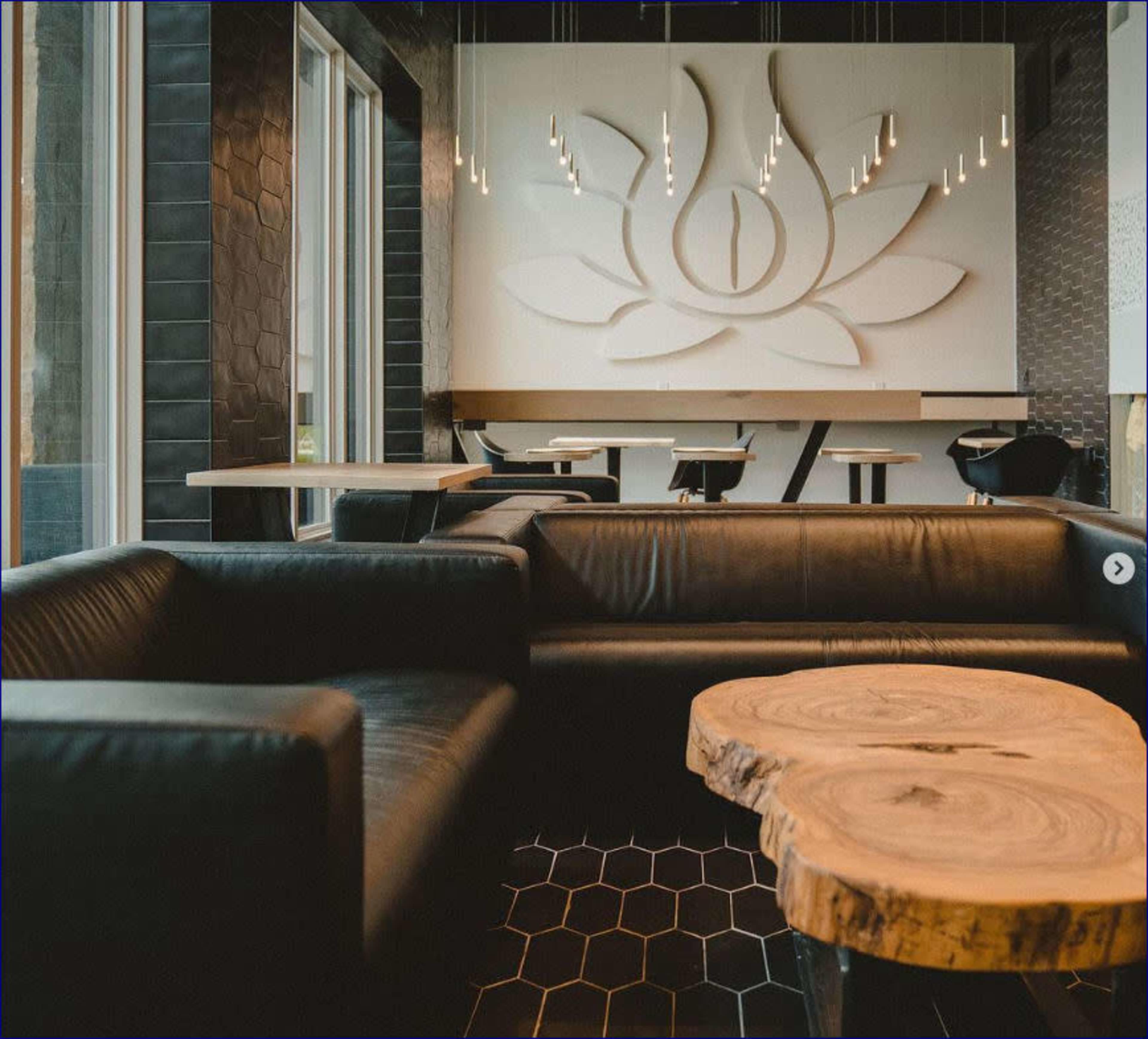 A black leather sofa and a wooden table are positioned in a modern interior featuring a large lotus flower design on the wall.