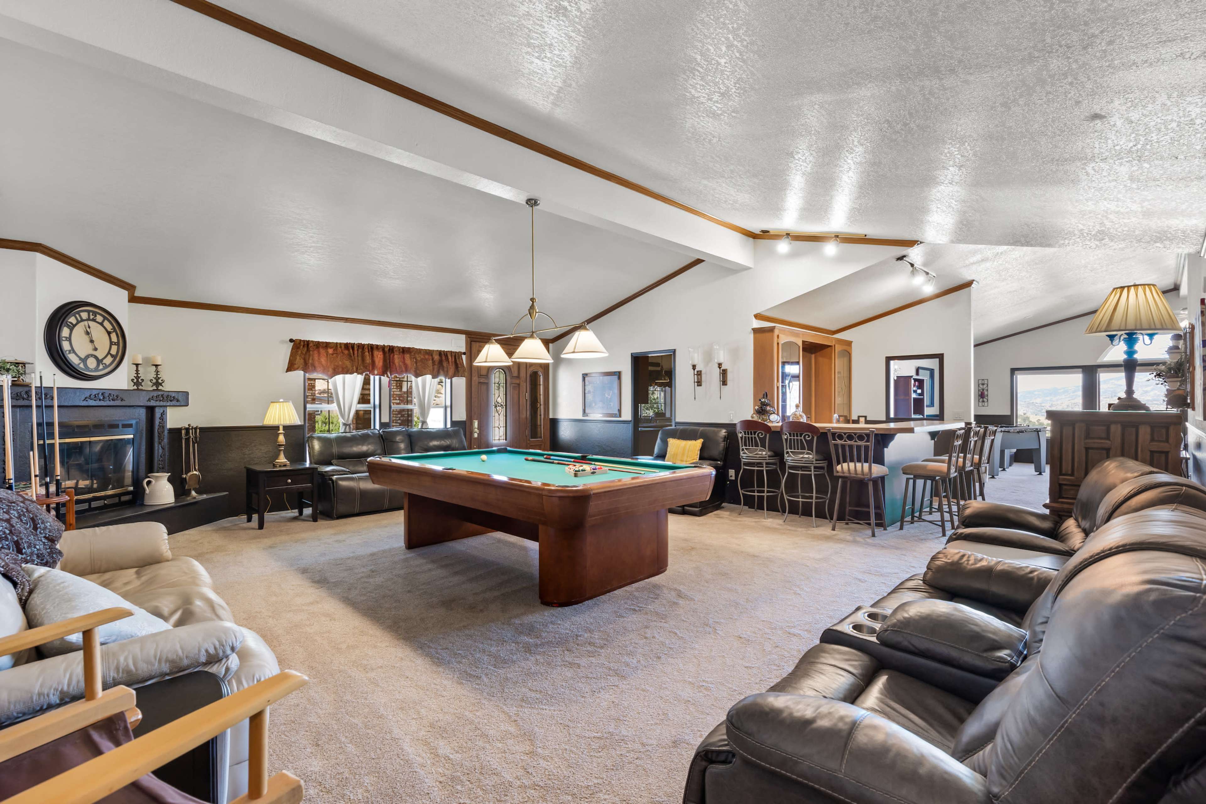 The spacious living area features a billiard table at the center, surrounded by seating options and a bar in the background.