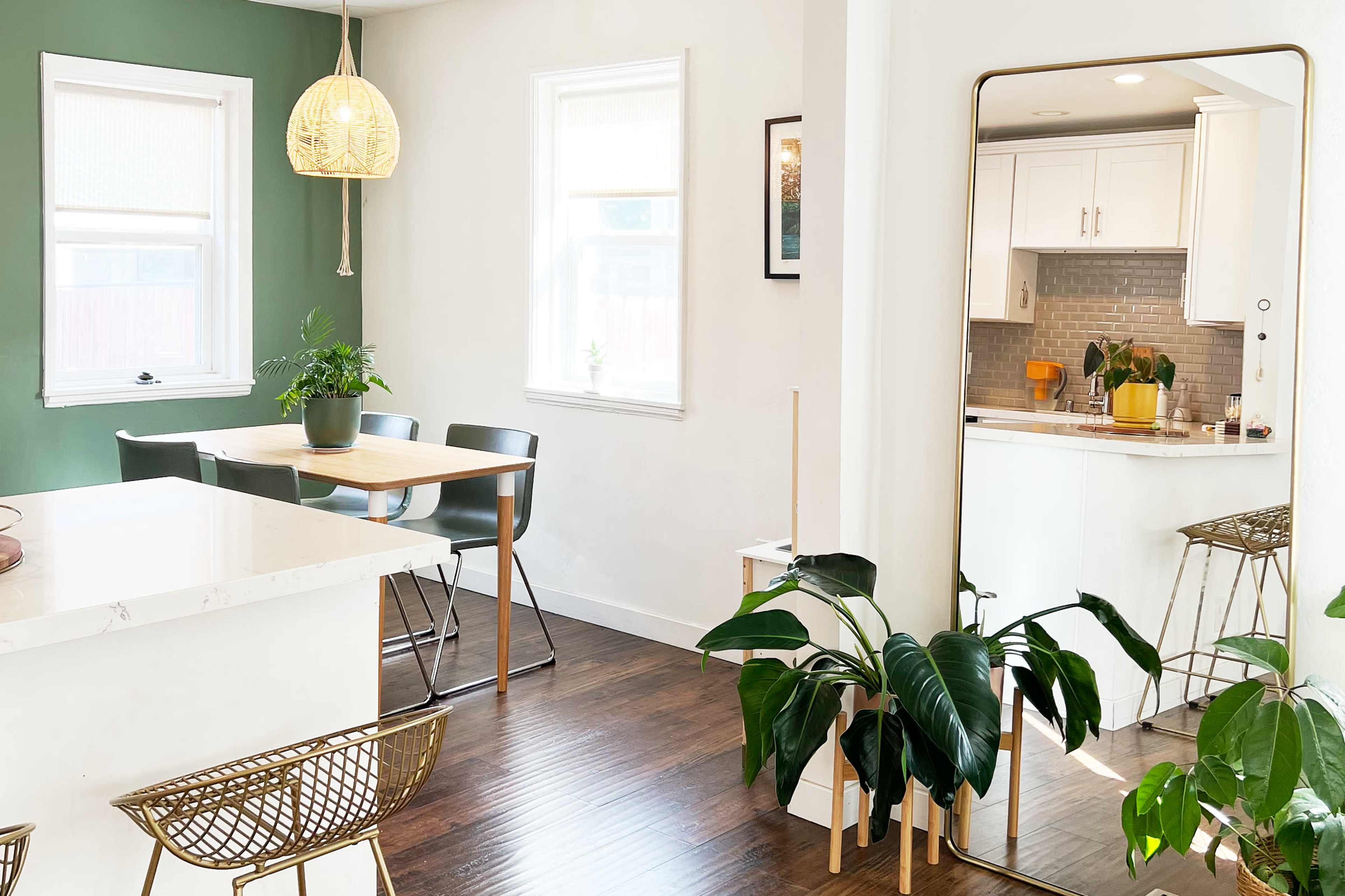 A modern kitchen and dining area featuring a wooden table with black chairs, a large mirror, and various houseplants.