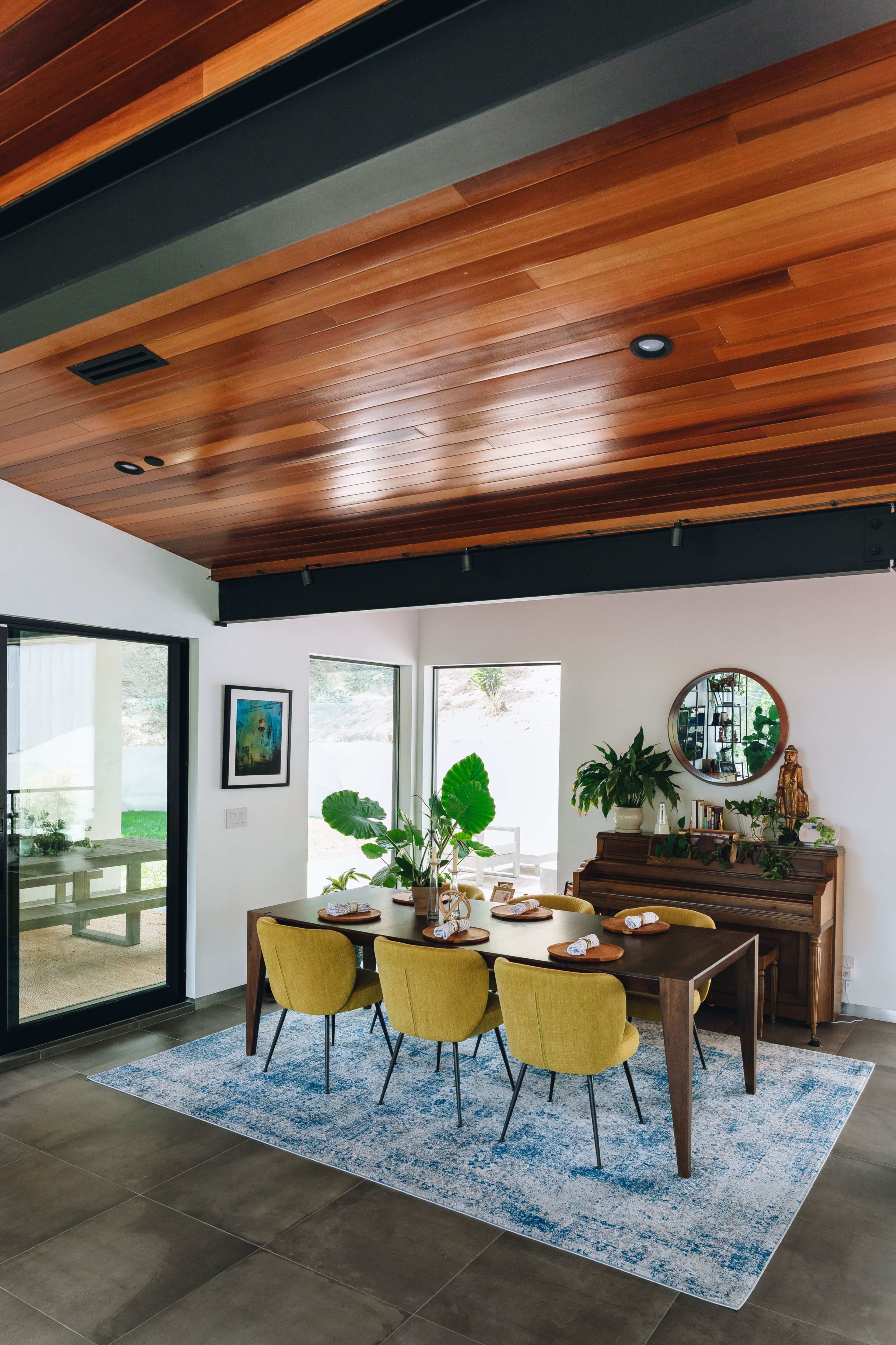 A dining area features a wooden table set for a meal, surrounded by yellow chairs and adorned with plants and decor.