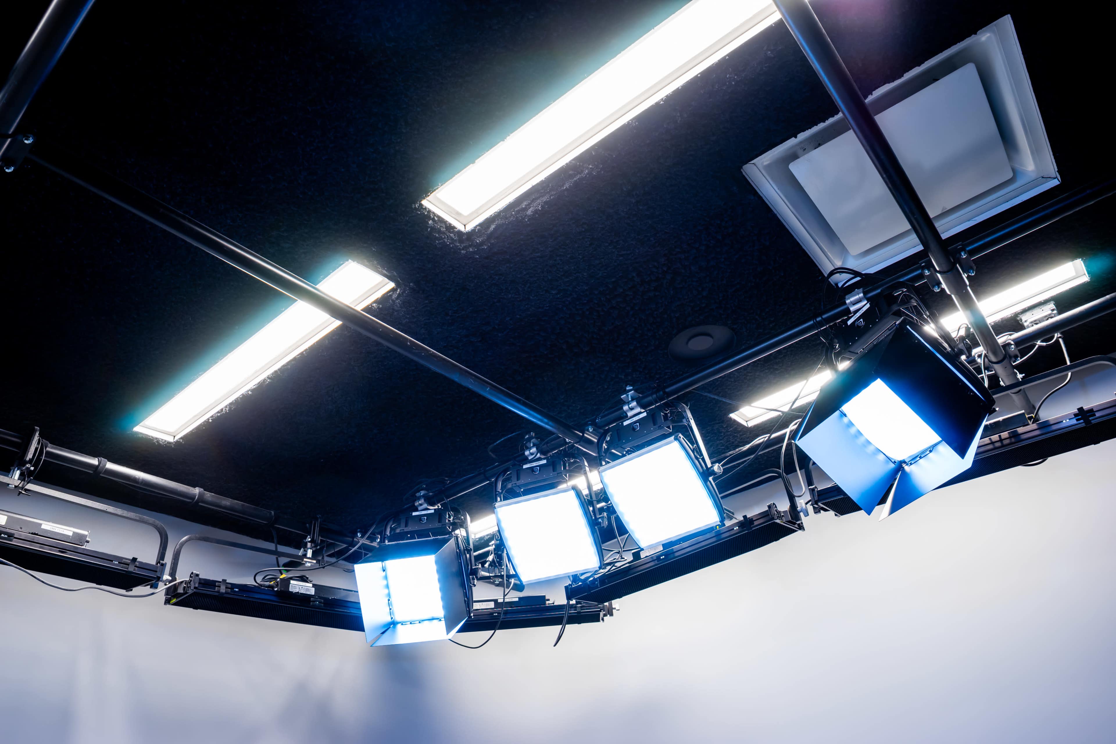 The image shows a ceiling with multiple lighting fixtures, including spotlights and fluorescent lights, arranged on metal tracks above a blank wall.