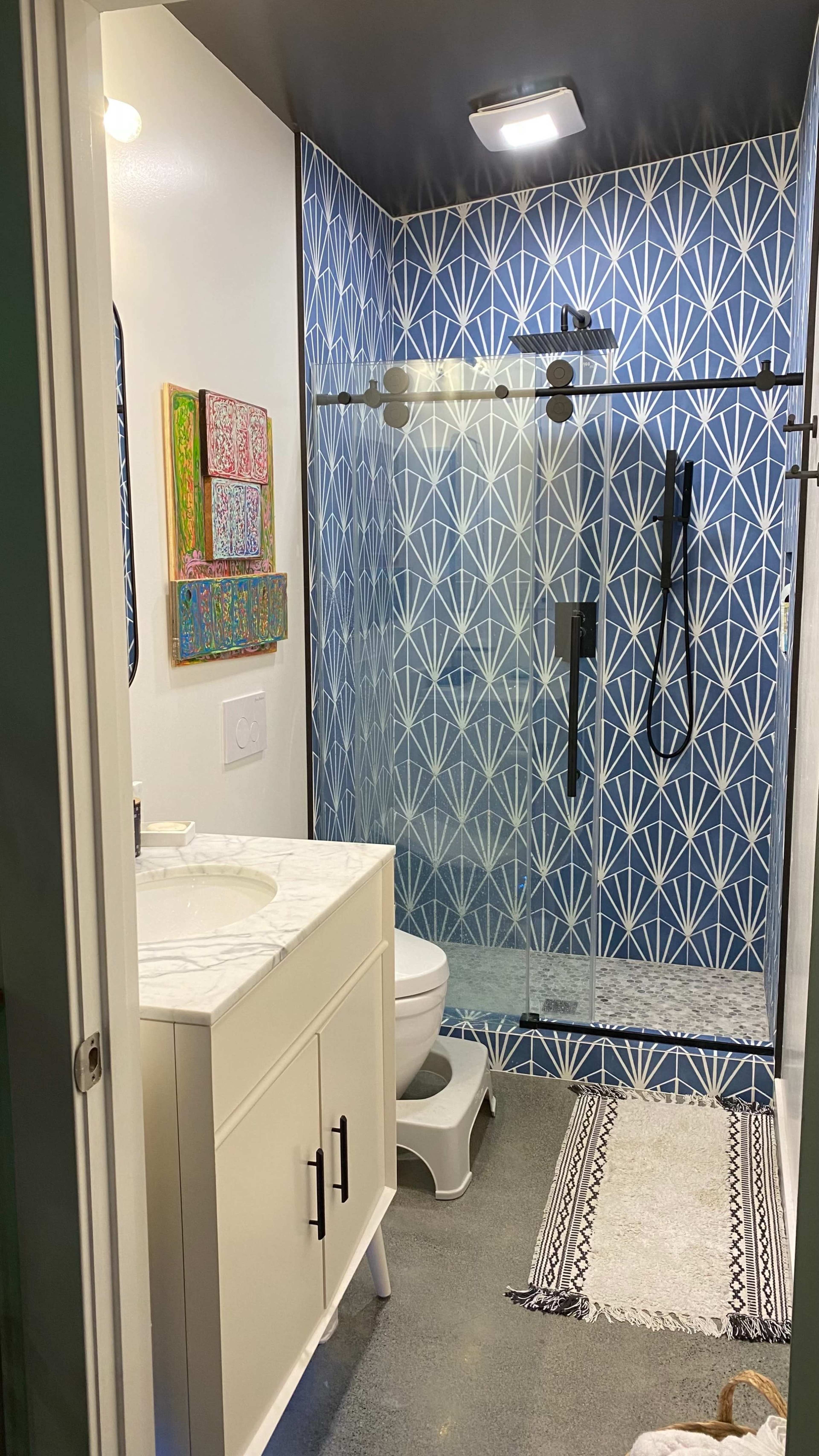A modern bathroom featuring a glass shower, a white vanity with a marble top, and a blue geometric-patterned accent wall.