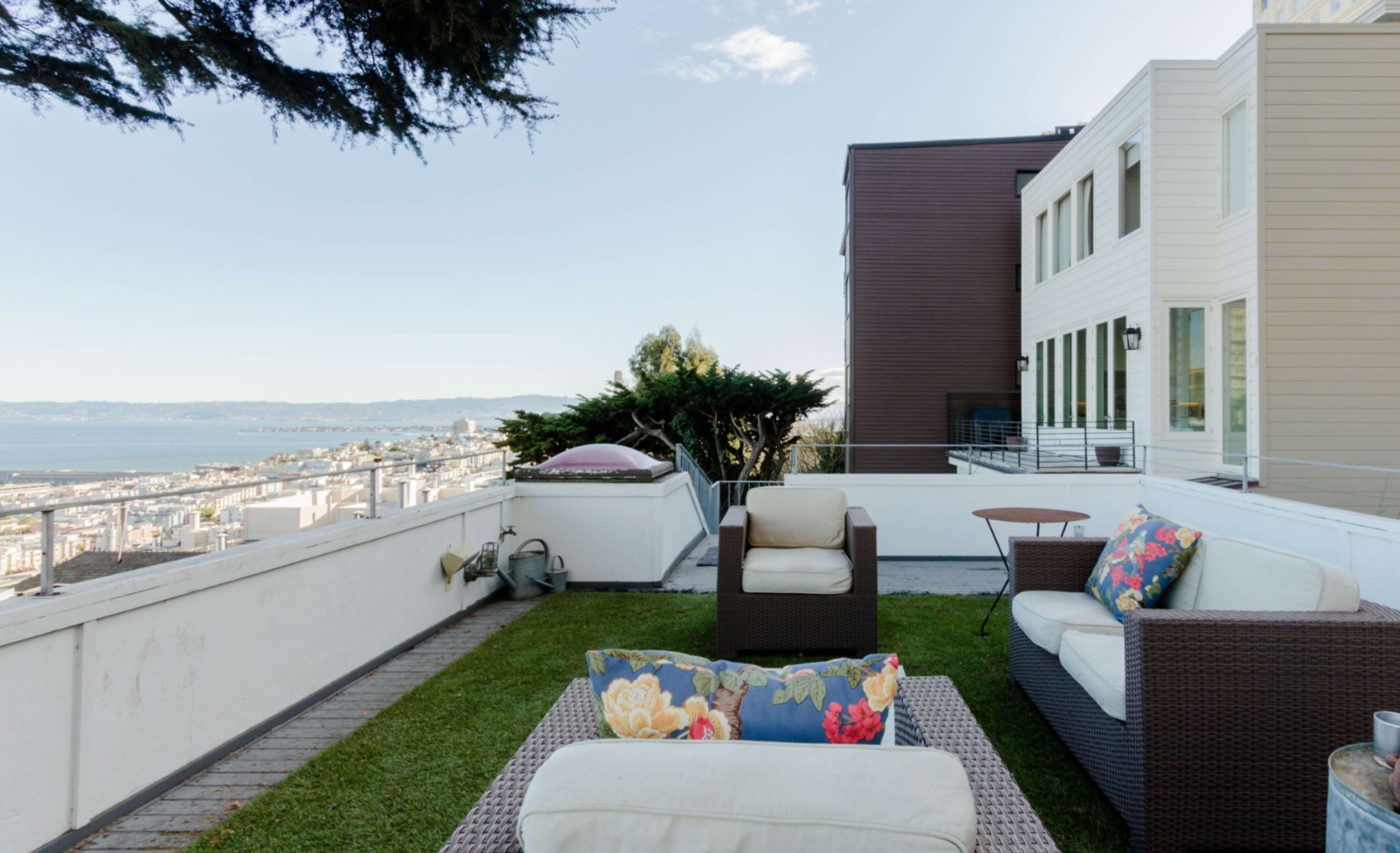 A terrace features two lounge chairs with colorful cushions, overlooking a panoramic view of a city and bay.