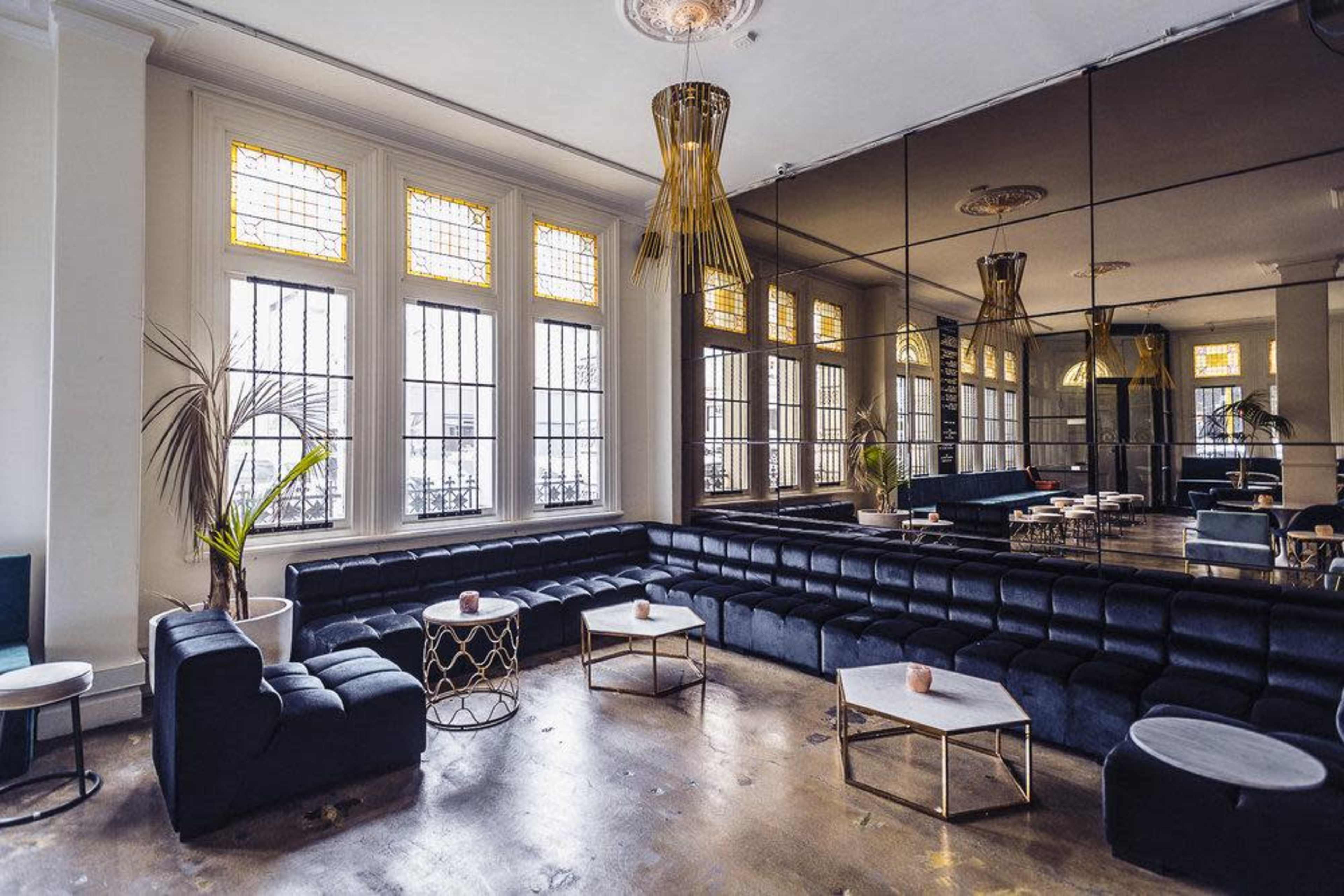 A modern lounge area with black seating, large windows featuring stained glass, and mirrored walls.