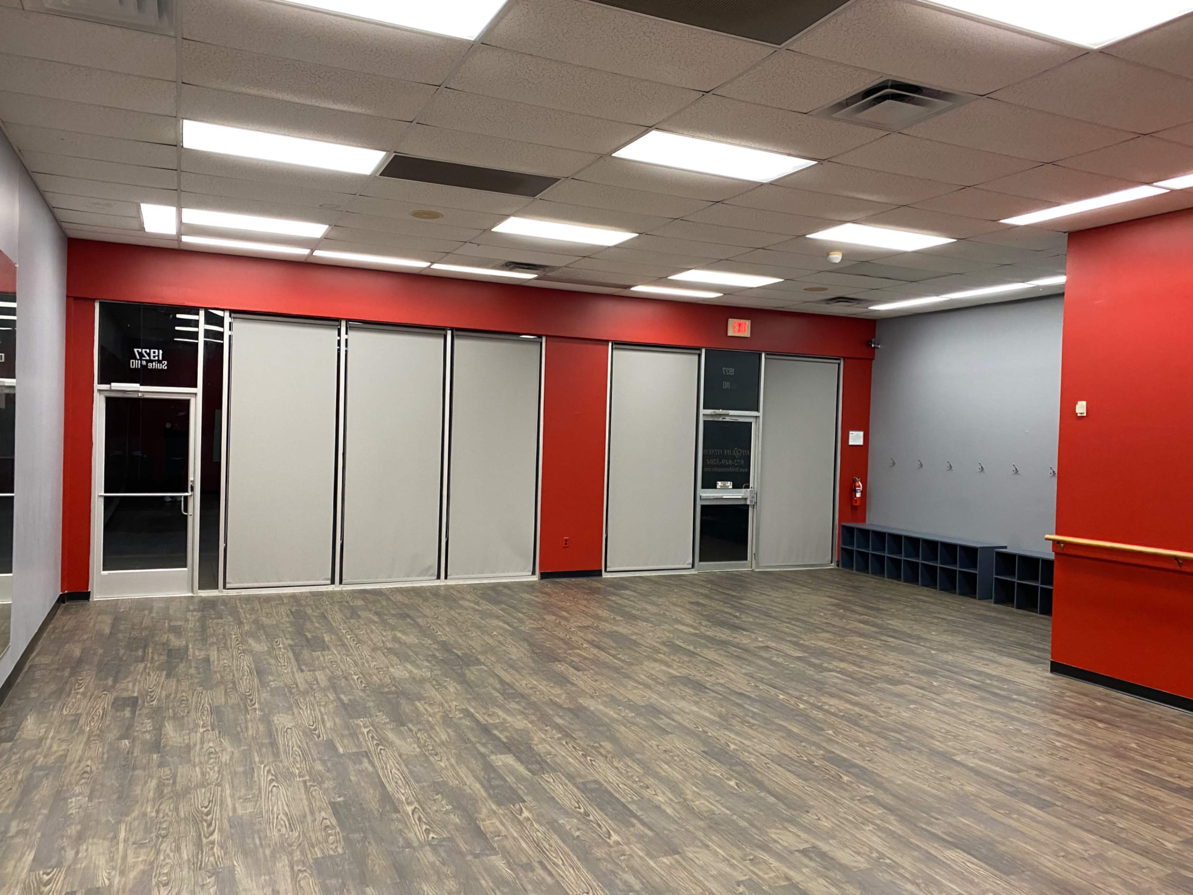 An empty room with red walls, gray curtains, and a wooden floor, featuring an entrance on one side and a row of hooks on the other.