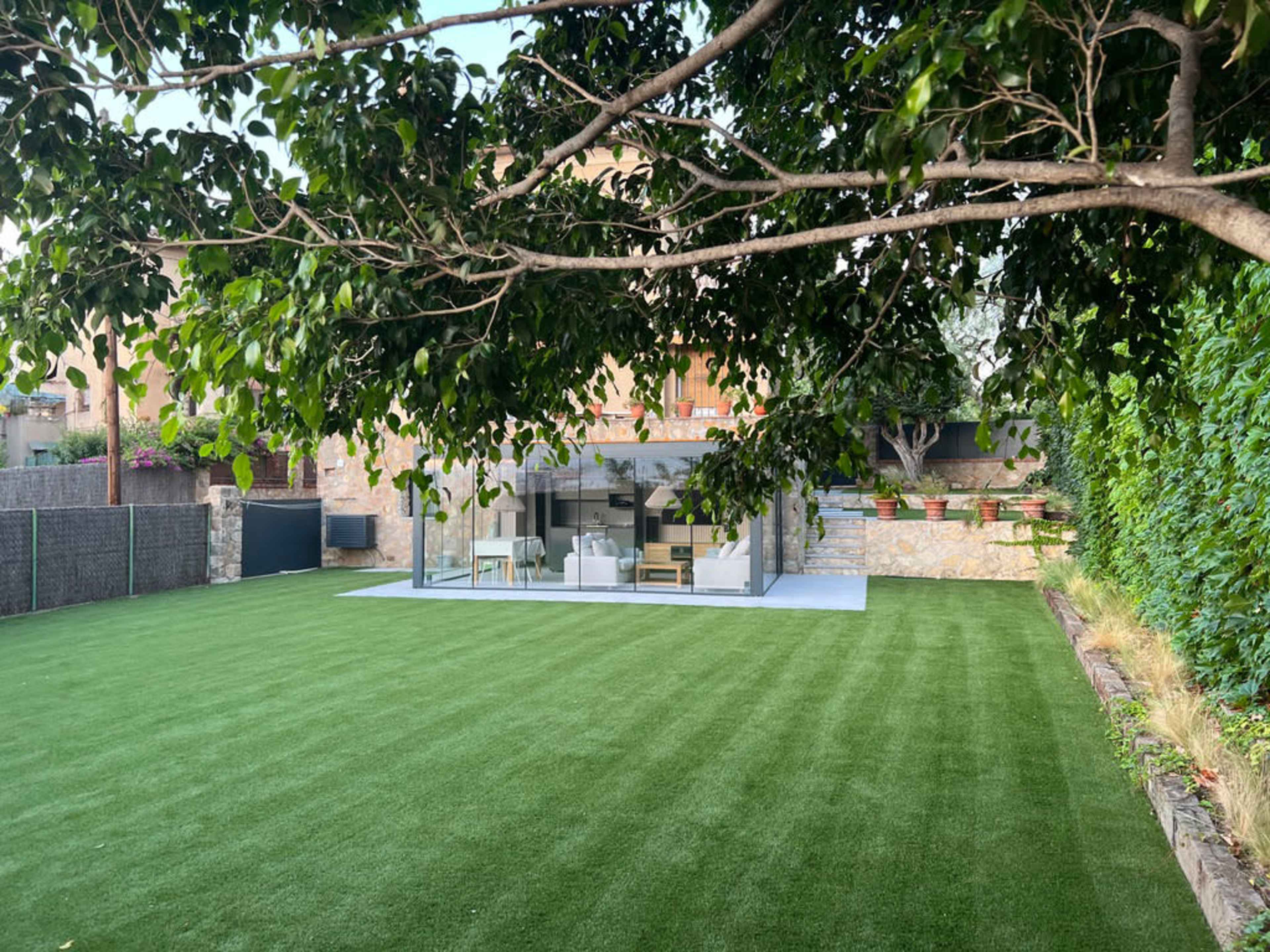 The image shows a landscaped garden with artificial turf and a modern glass-walled structure in the background.