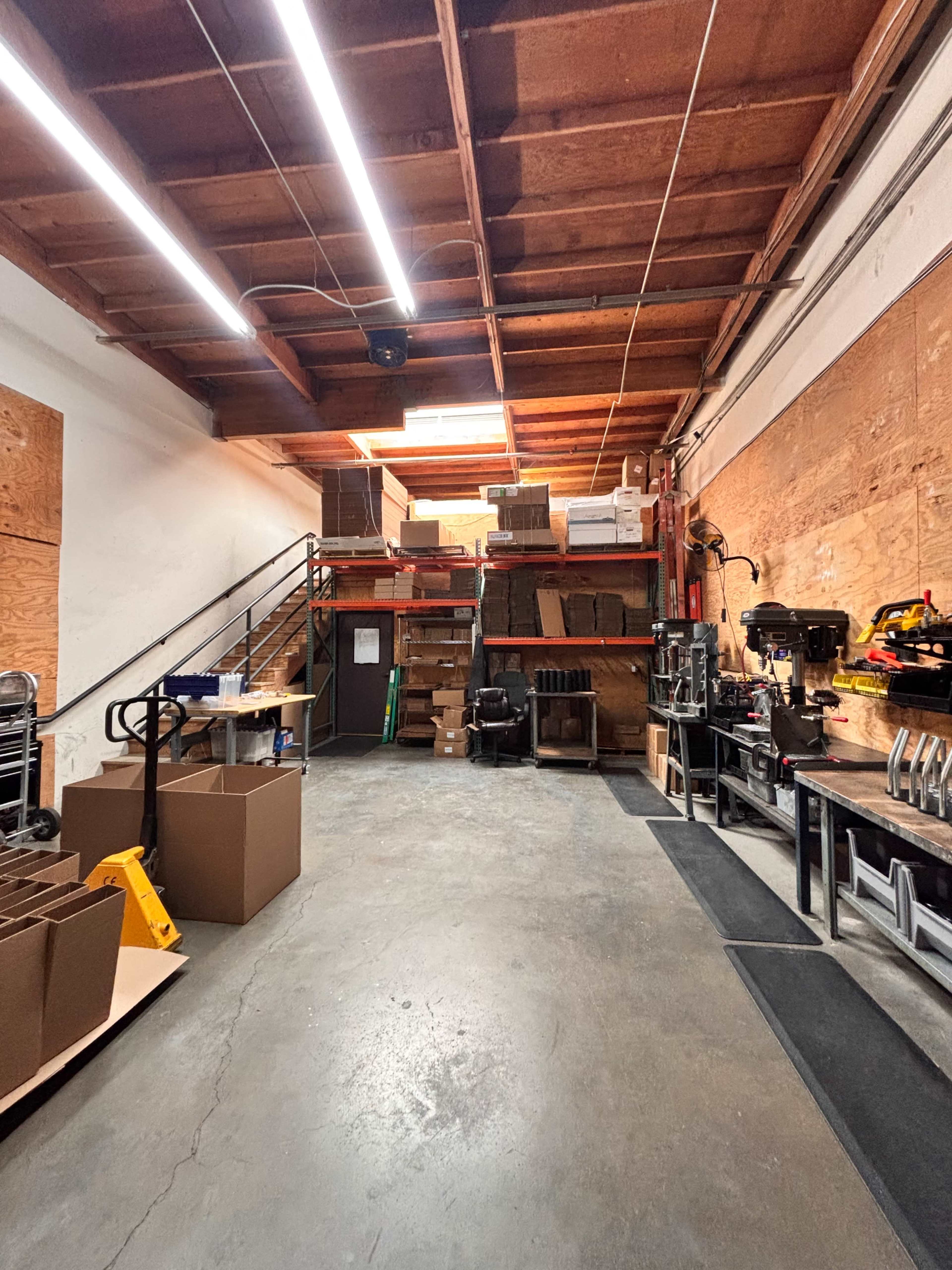 The image shows a spacious warehouse interior with stacked boxes and various equipment along the walls.