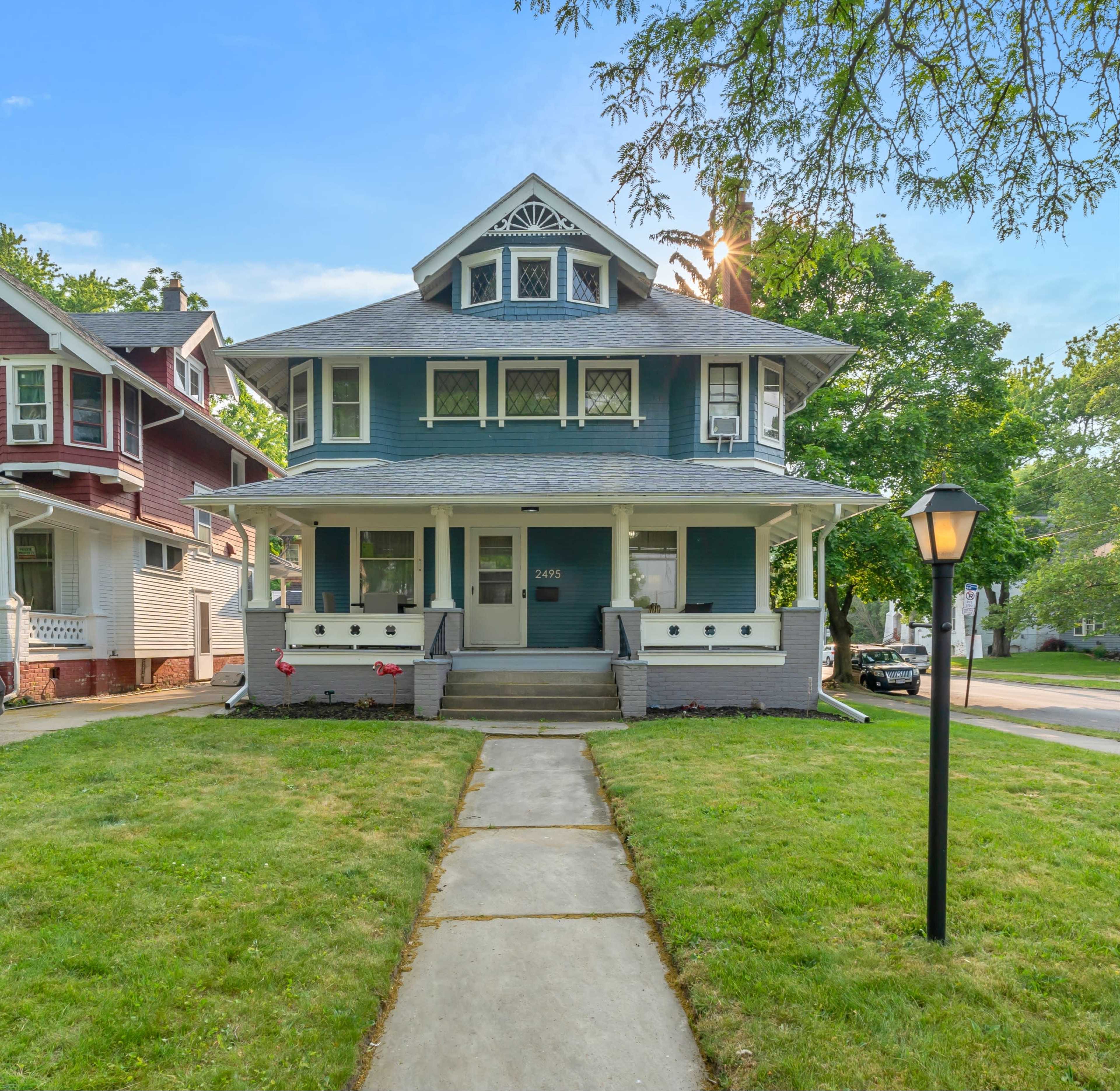 A two-story blue house with a steeply pitched roof, a front porch, and a manicured lawn.