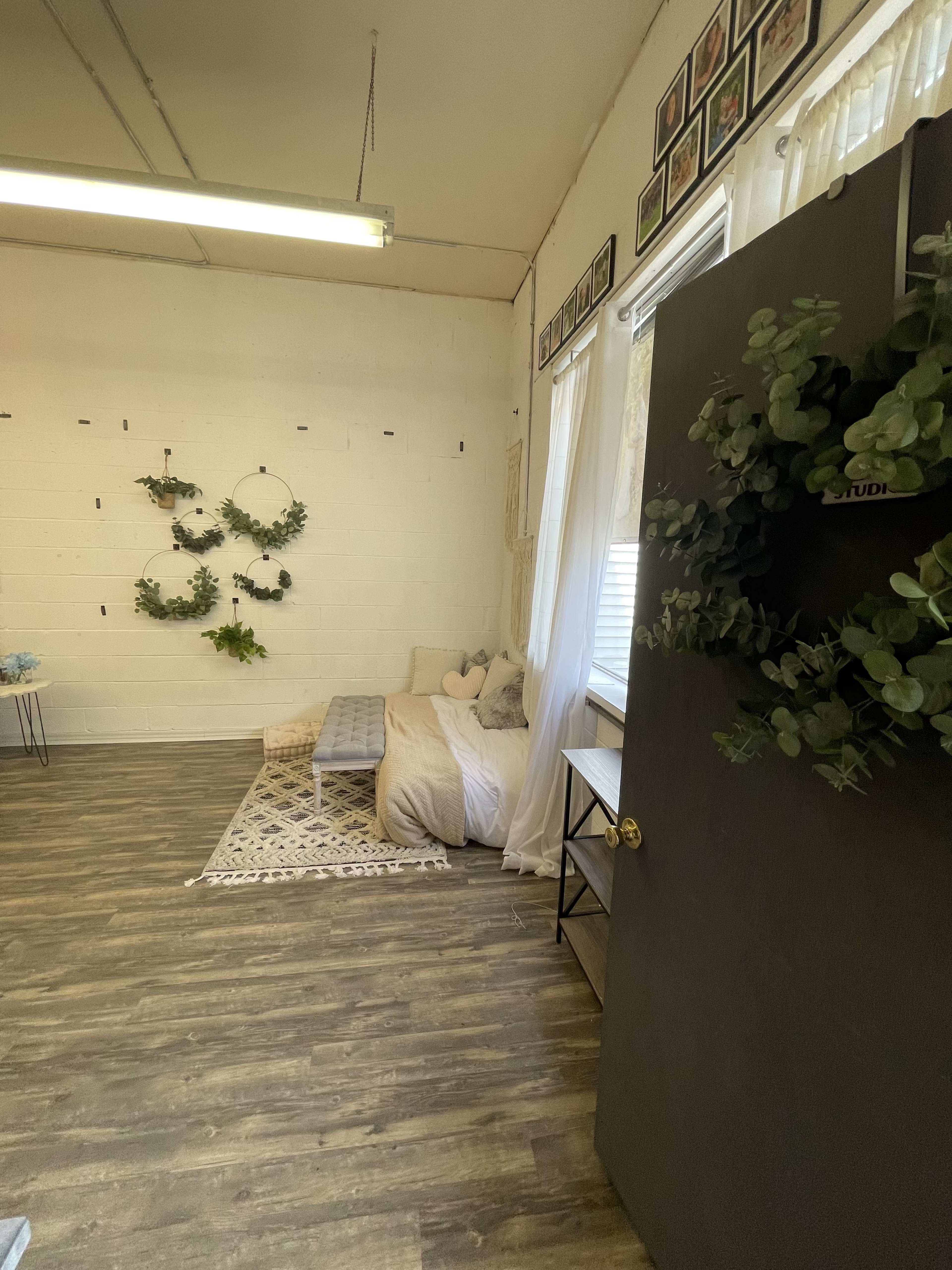 A room with a seating area featuring a couch, decorative wall hangings with plants, and a door adorned with a wreath.