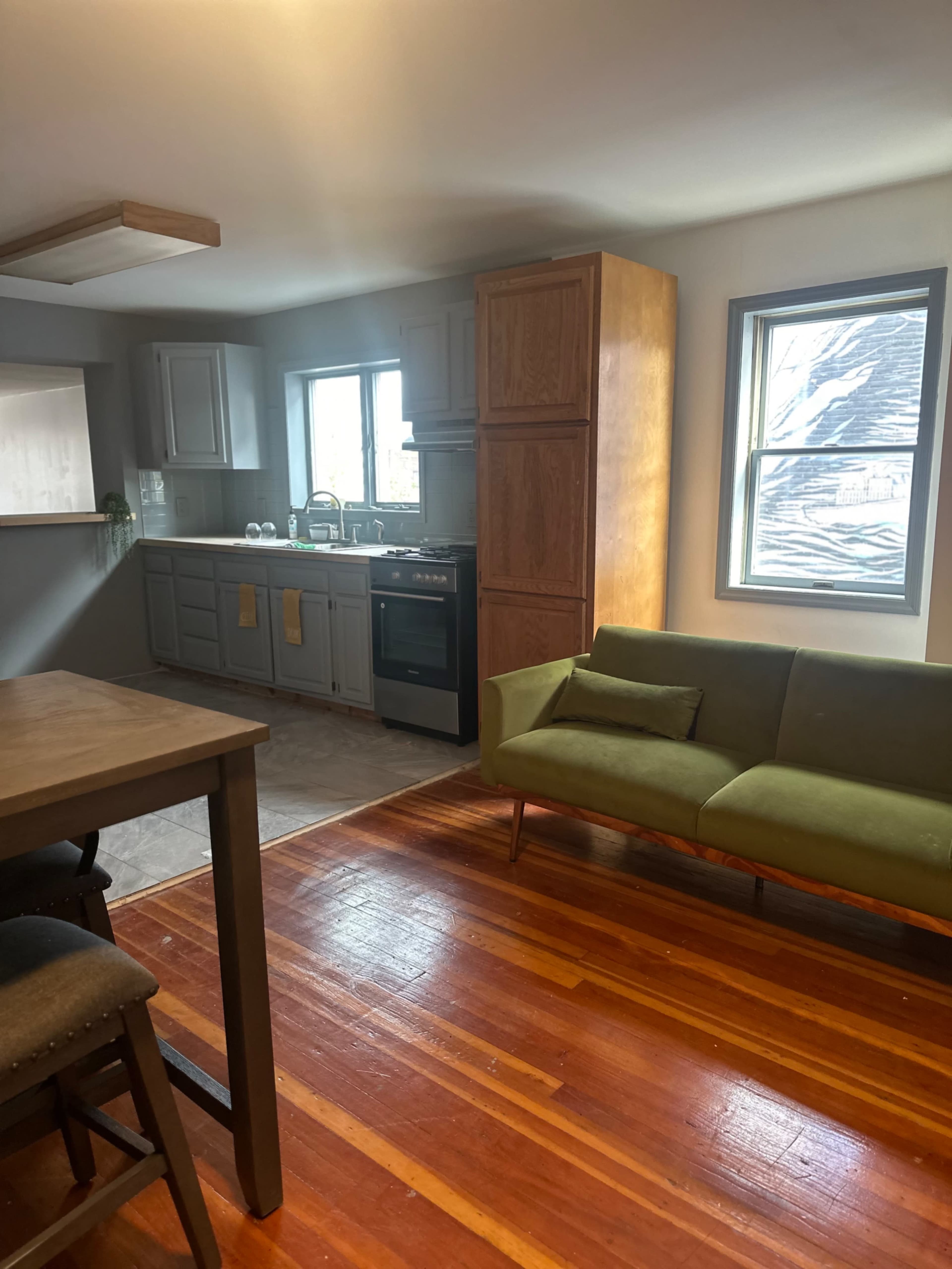 A kitchen and living area featuring wooden floors, a green couch, and cabinetry with a stove and sink.