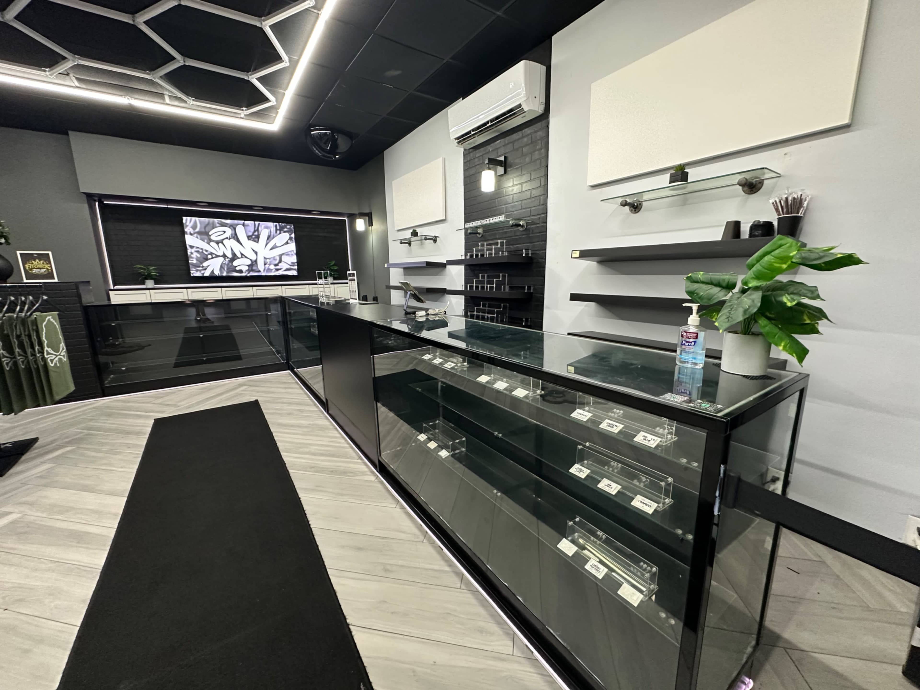 The image shows a modern retail space featuring a glass display counter, shelving, and a digital screen on the wall.