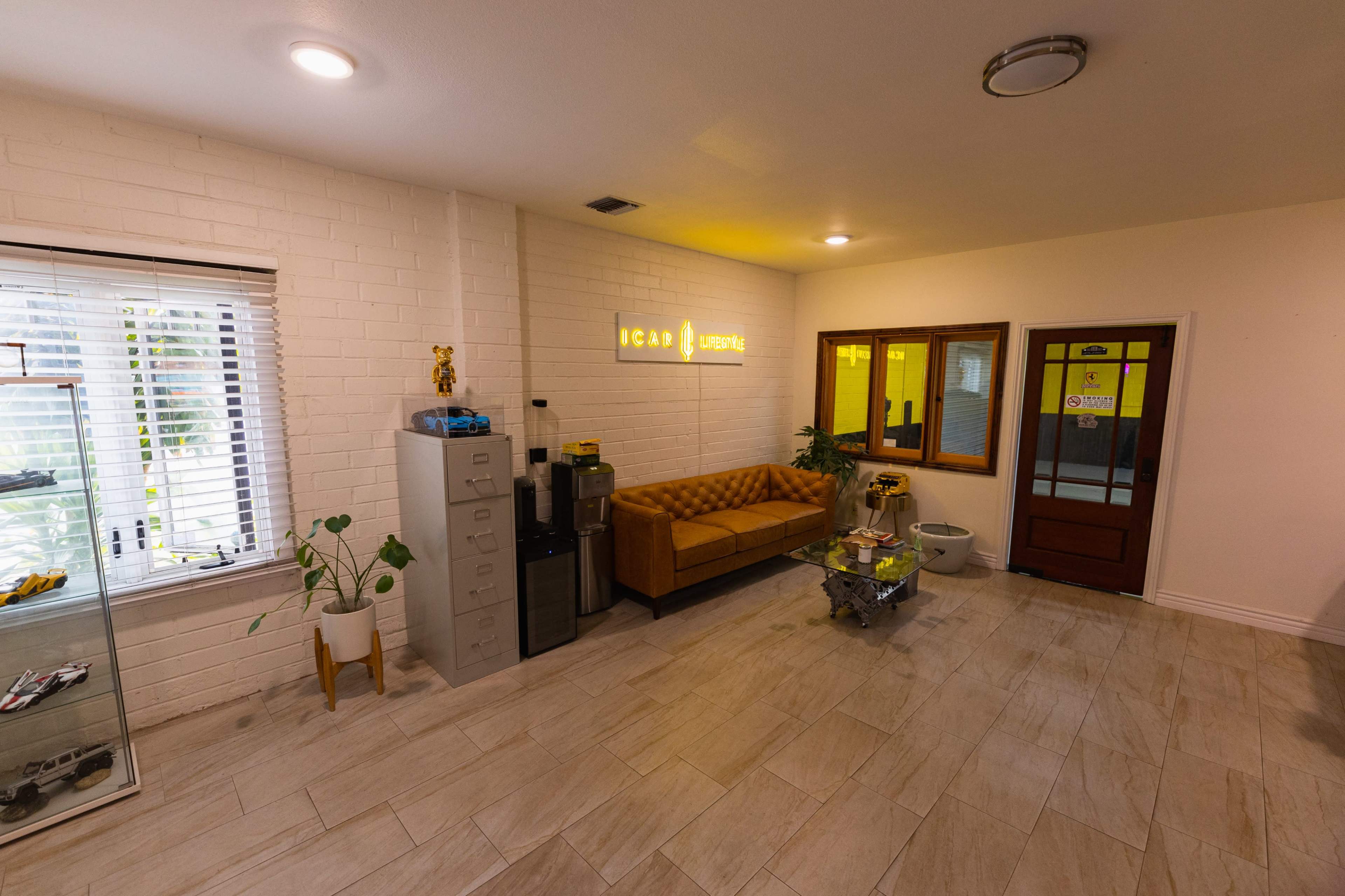 The image shows a small, well-lit reception area with a brown leather sofa, filing cabinets, and glass doors leading to other rooms.