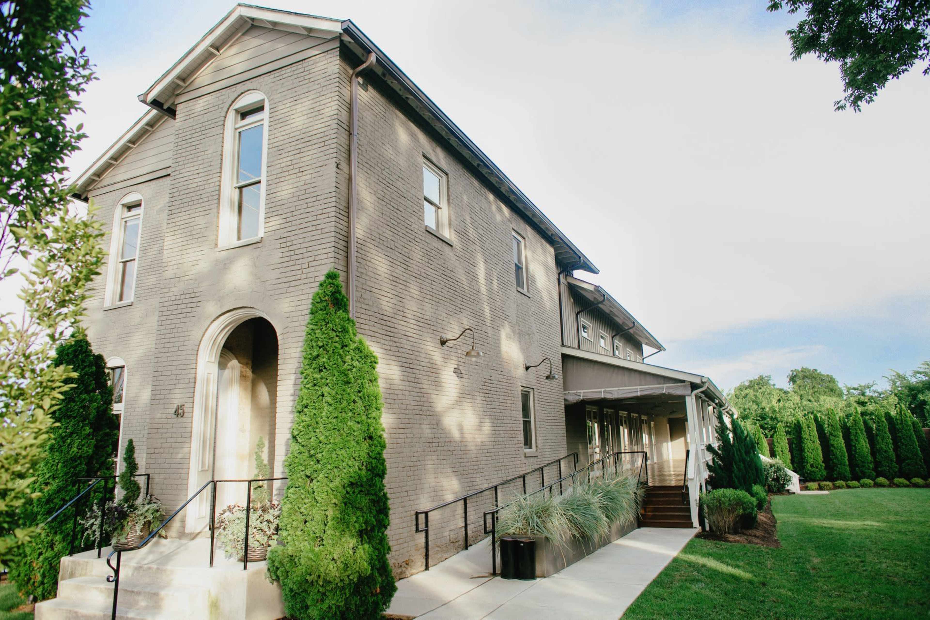 A two-story gray brick house features a prominent entrance and neatly landscaped greenery in the front yard.