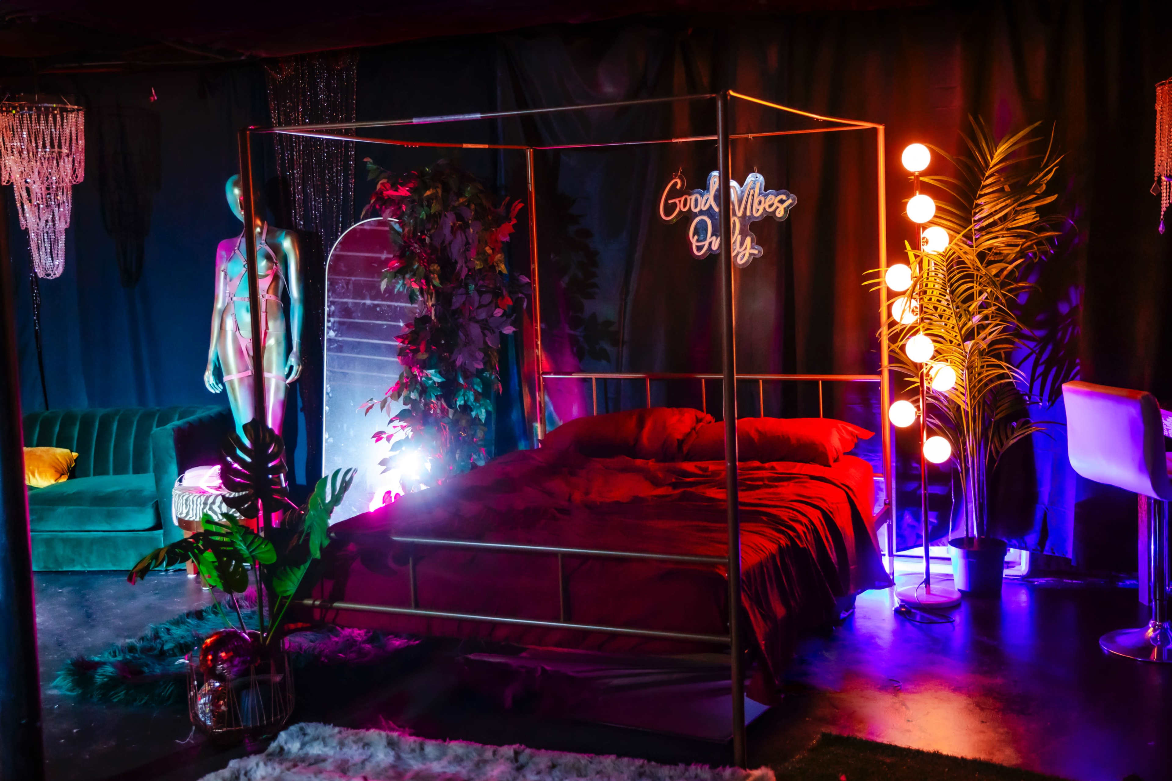 A modern bedroom with a metallic bed frame, colorful lighting, a neon sign, and decorative plants.