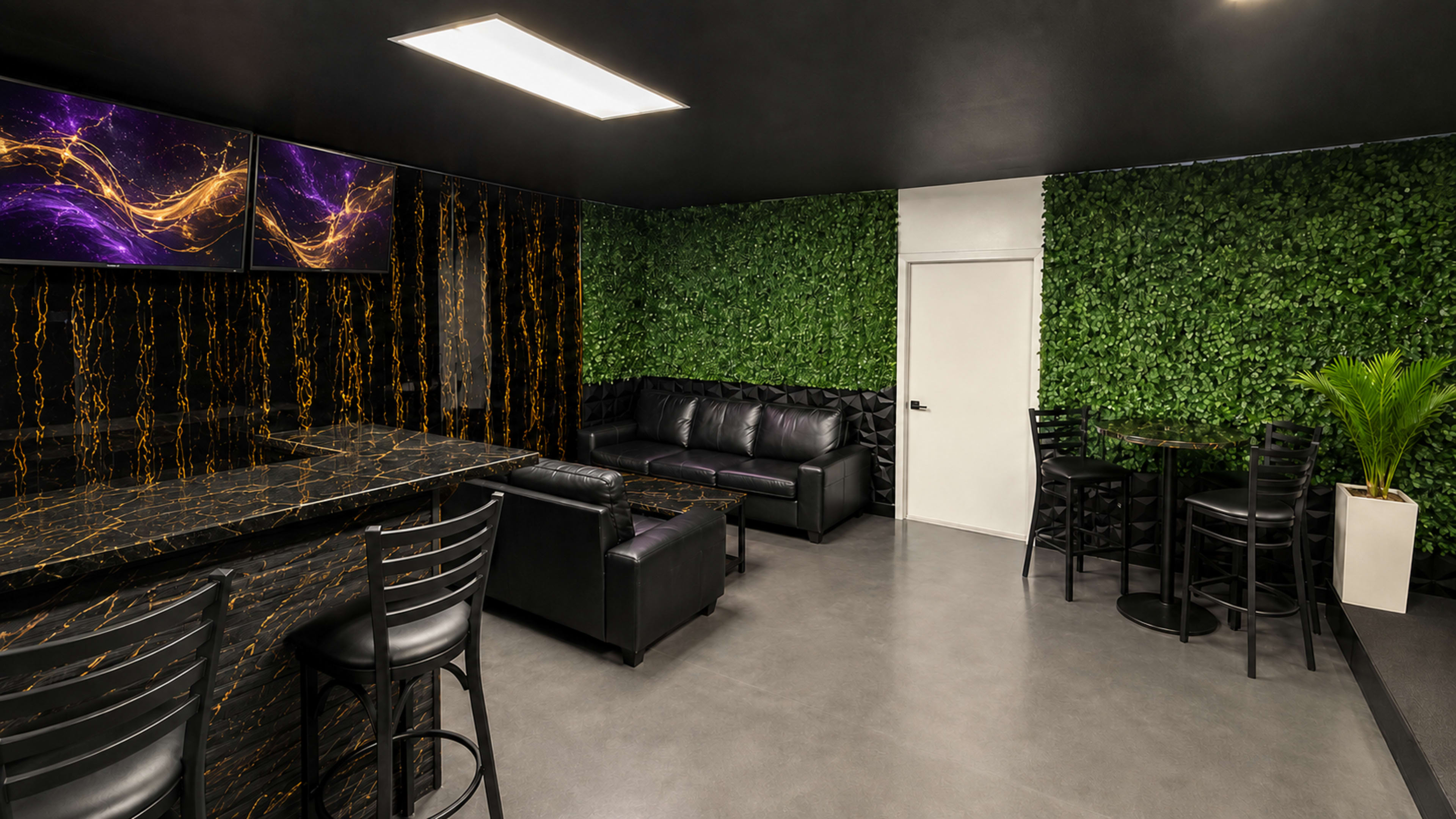 The image shows a modern lounge area featuring a black and gold marble bar, black leather couches, and a wall adorned with artificial greenery.
