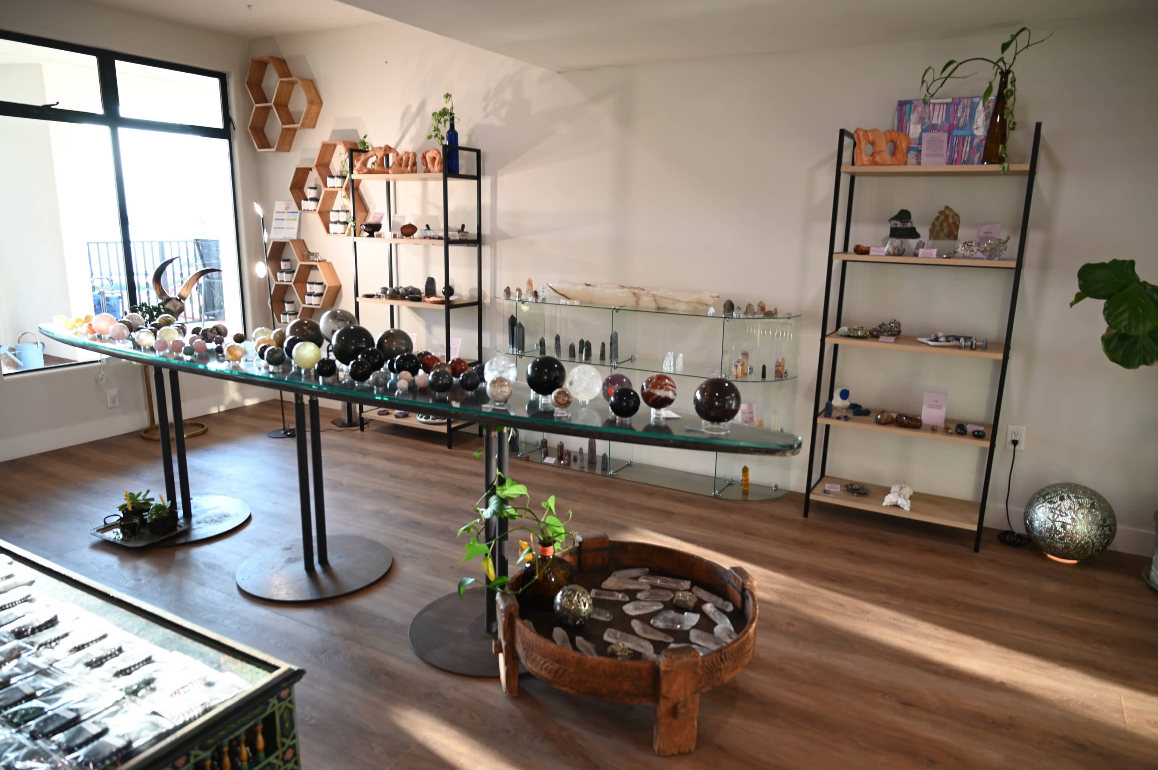The image shows a brightly lit interior displaying various decorative stones and crystals arranged on glass and wooden shelves.