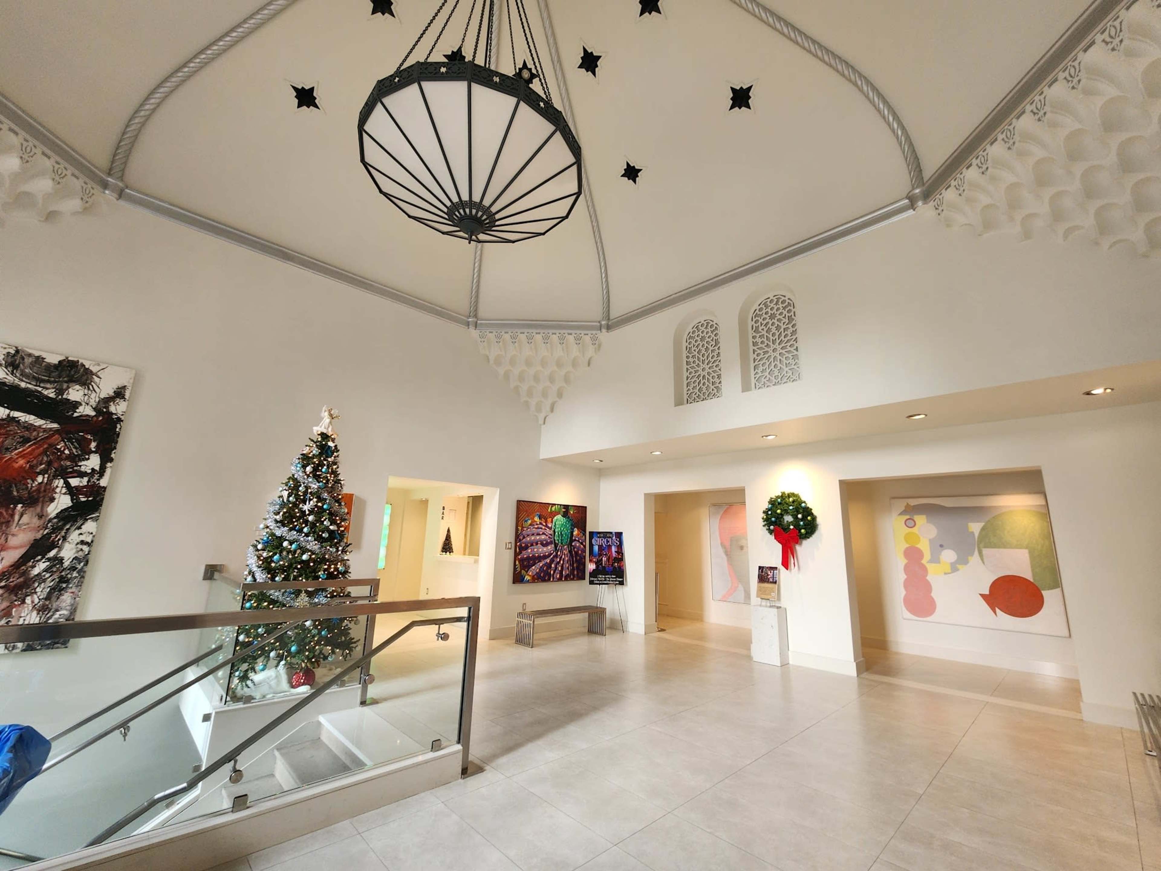 A spacious entryway features a large chandelier, a decorated Christmas tree, and artworks displayed on the walls.