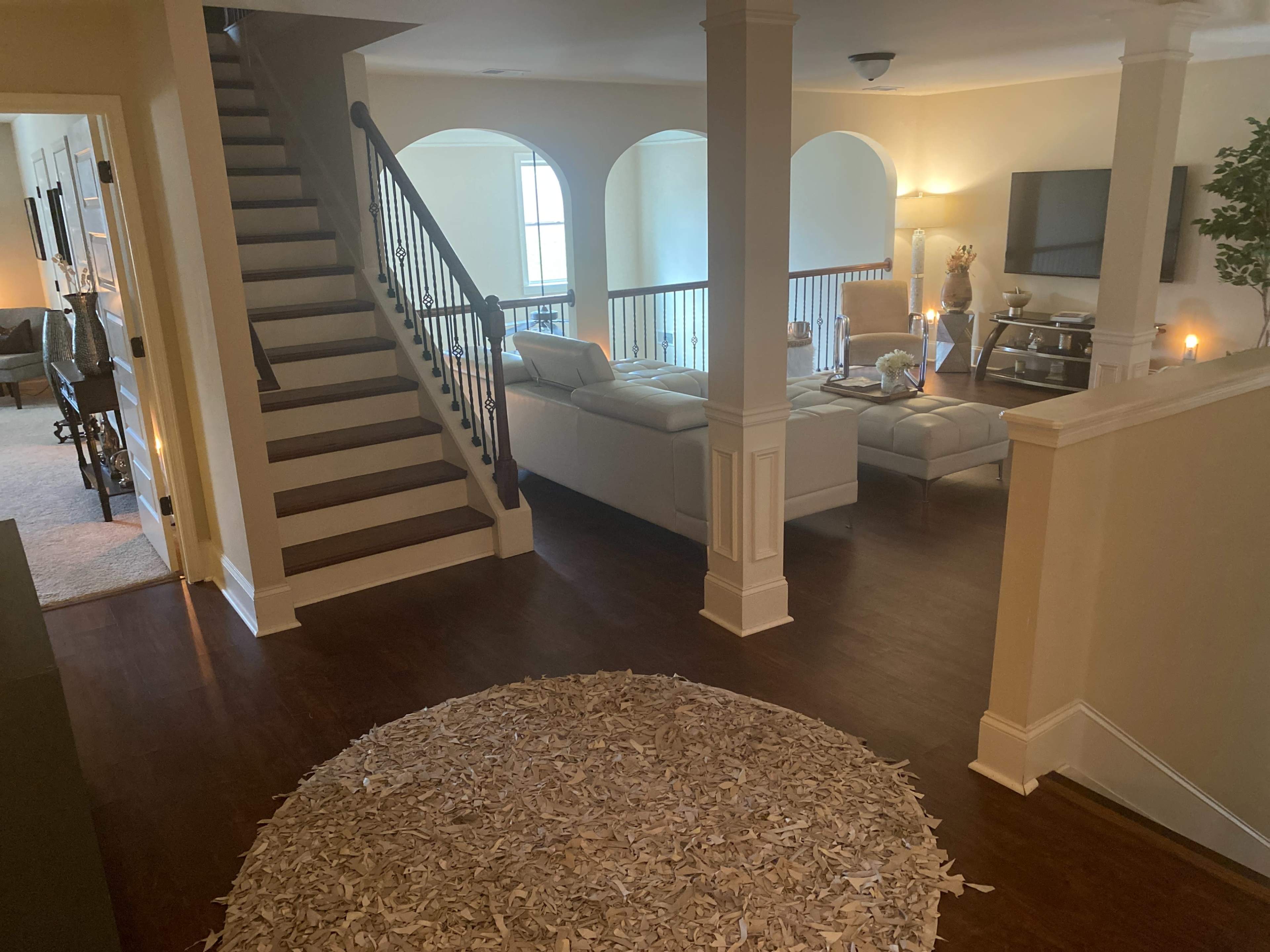 A well-lit foyer leads to a staircase and an open living area furnished with a white sectional sofa and a coffee table.