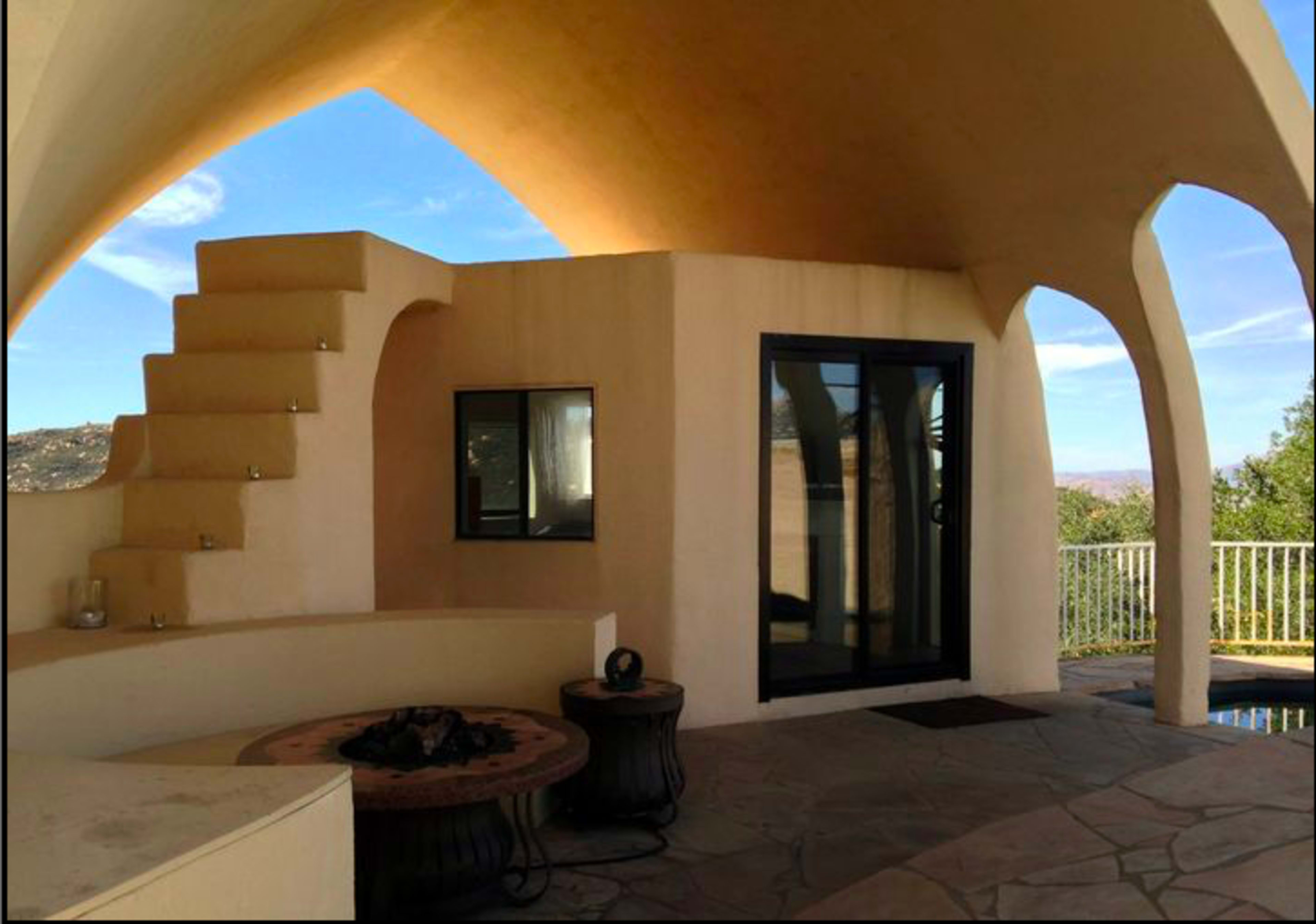 A modern architectural interior with a curved ceiling, a staircase leading up, and a large glass door opening to an outdoor view.