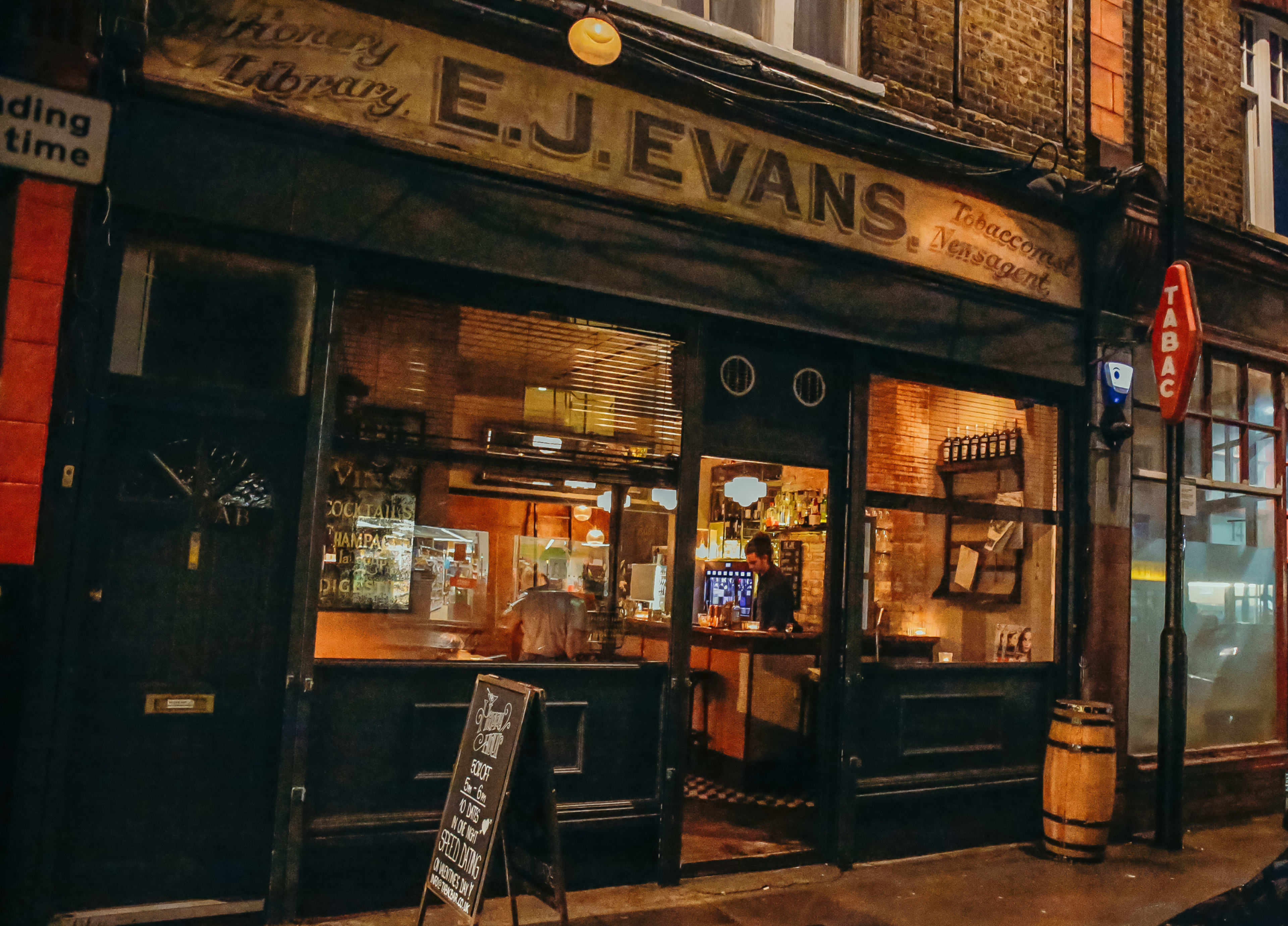 The image shows a night scene of a tavern called E.J. Evans, with its illuminated windows and a menu board outside.