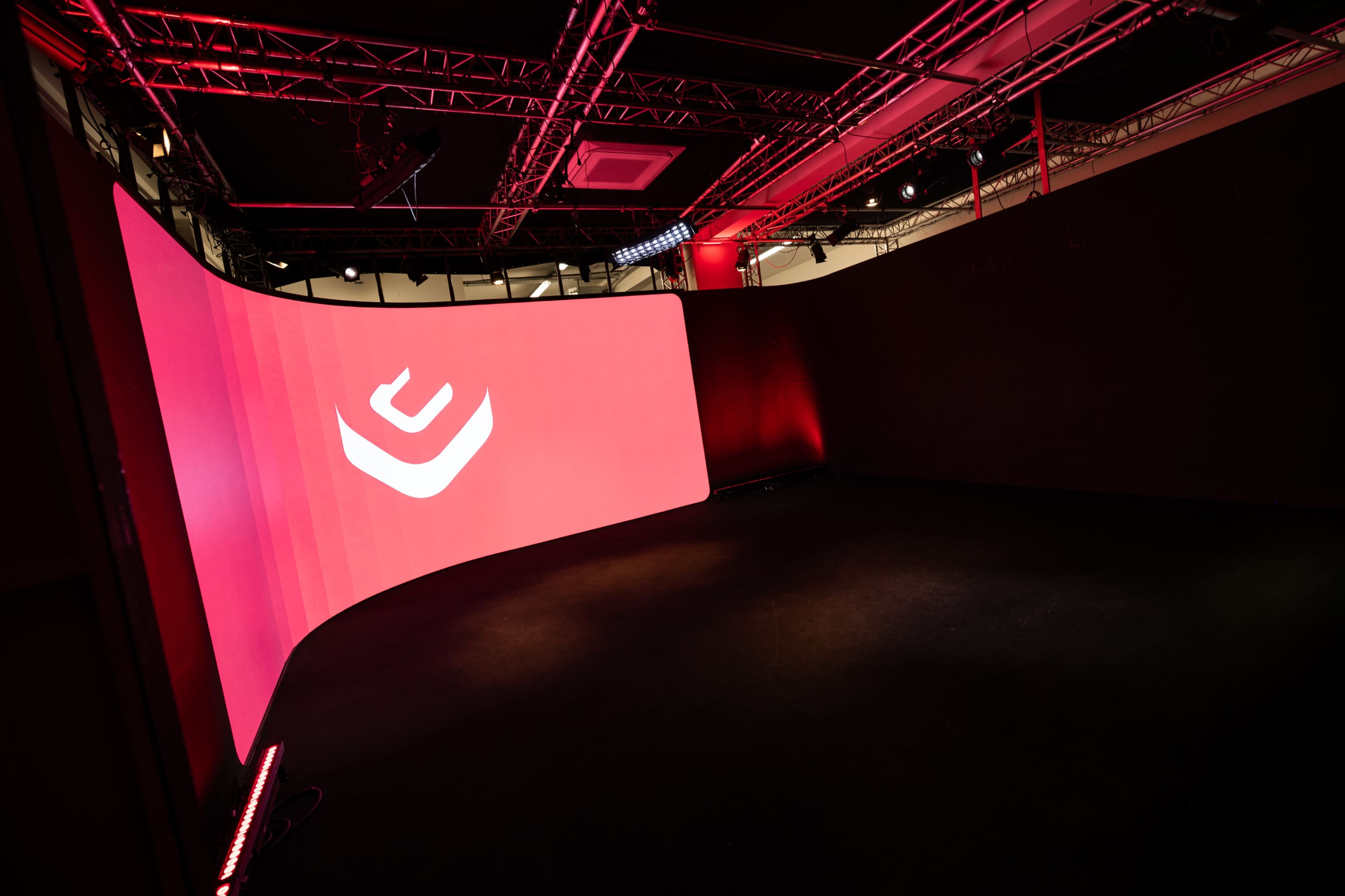 A curved red backdrop with a logo displayed on it in a dimly lit, enclosed space.