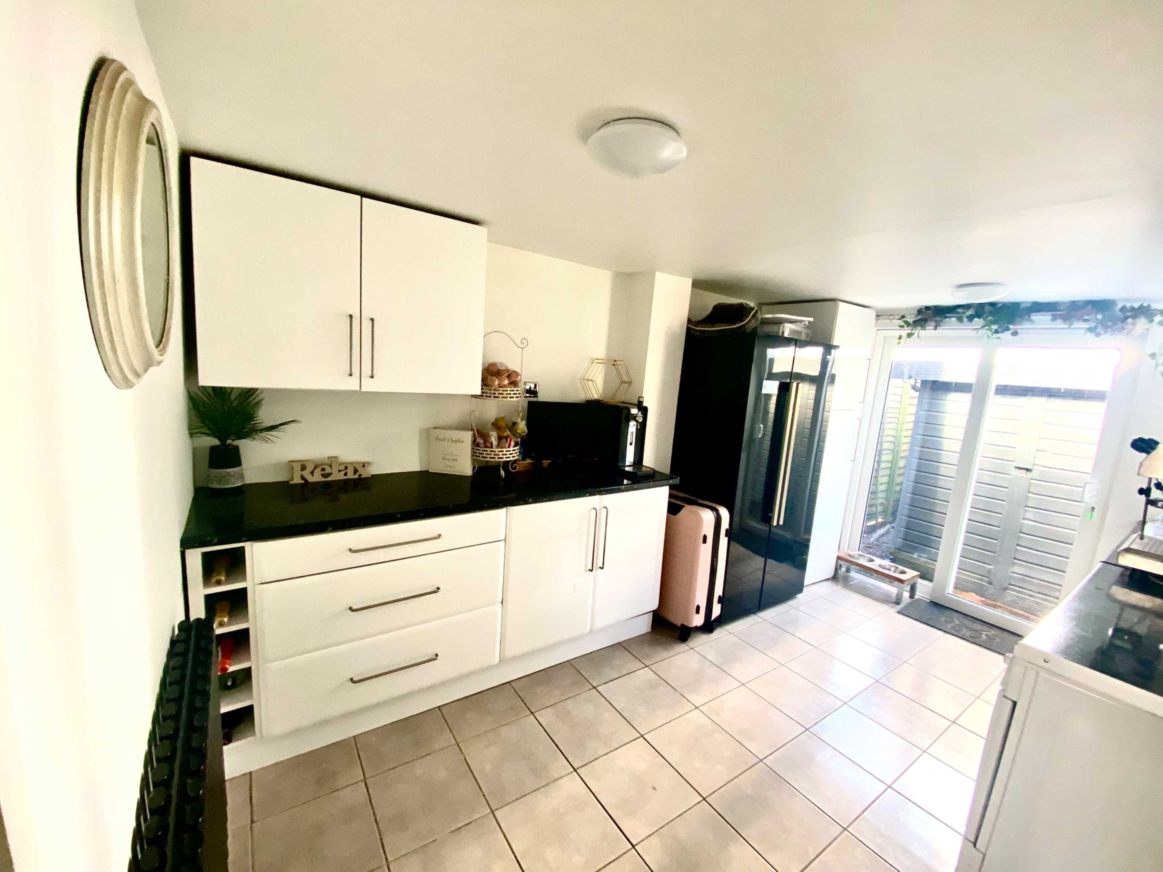 The image shows a modern kitchen with white cabinetry, a black countertop, and a door leading to an outdoor area.