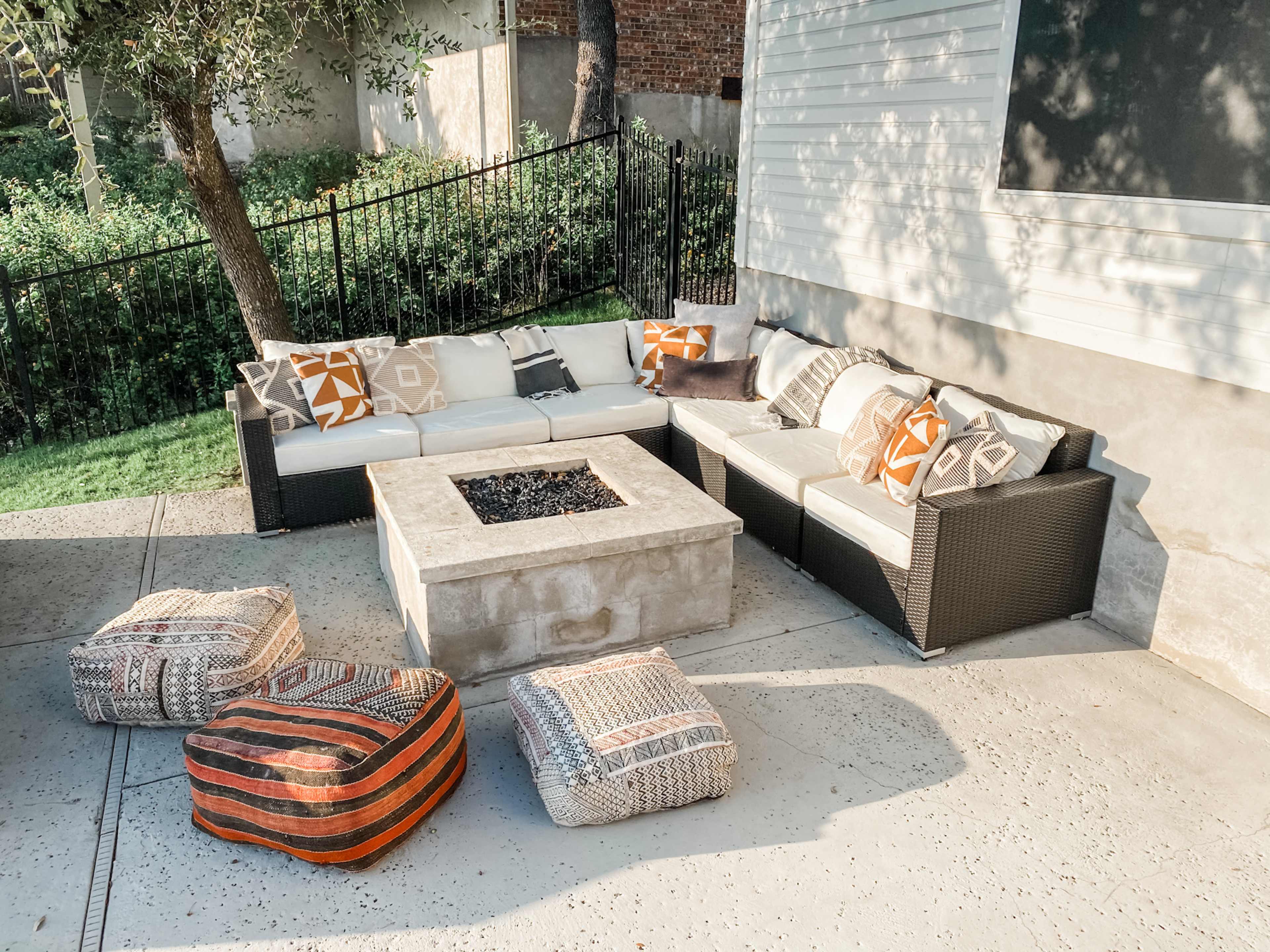 A patio area features a sectional sofa with decorative cushions and a rectangular fire pit surrounded by additional seating cushions.