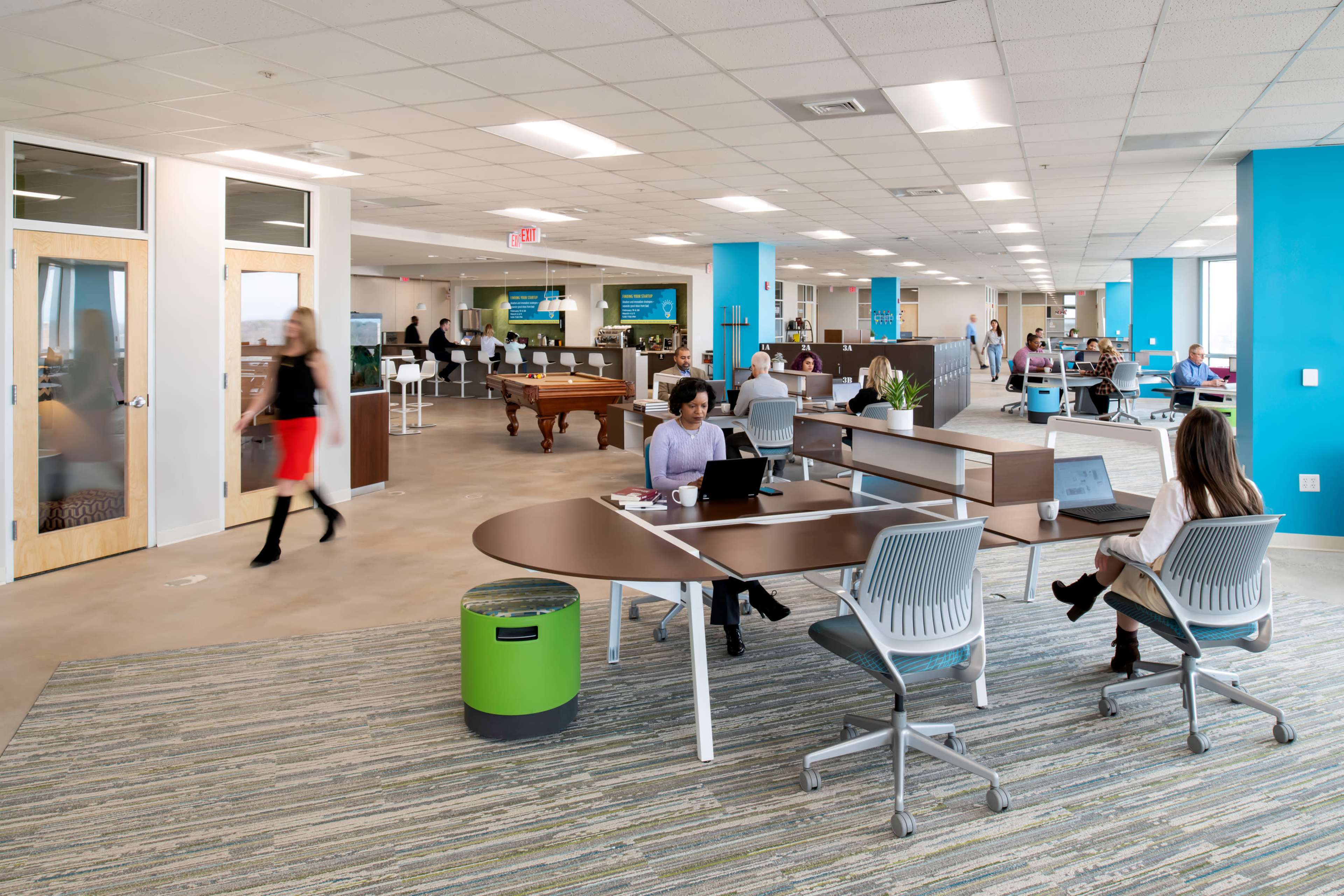 A modern office space featuring a mix of workstations, a lounge area with a pool table, and employees engaging in various activities throughout the room.