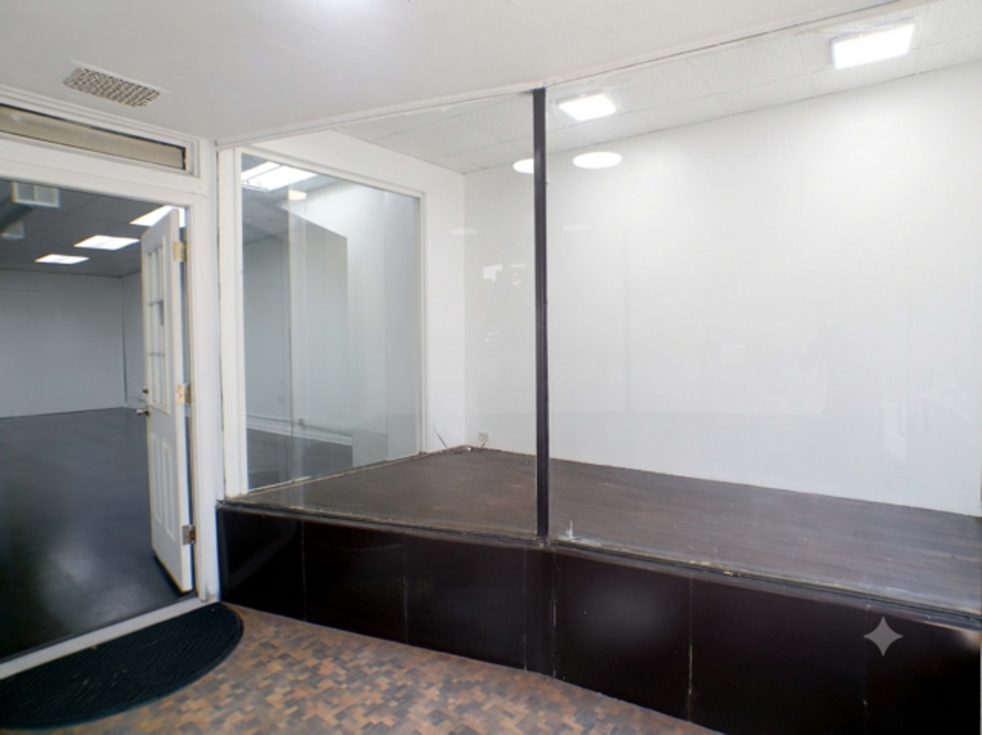The image shows an empty retail space with a glass front, a wooden platform, and a white wall in the background.